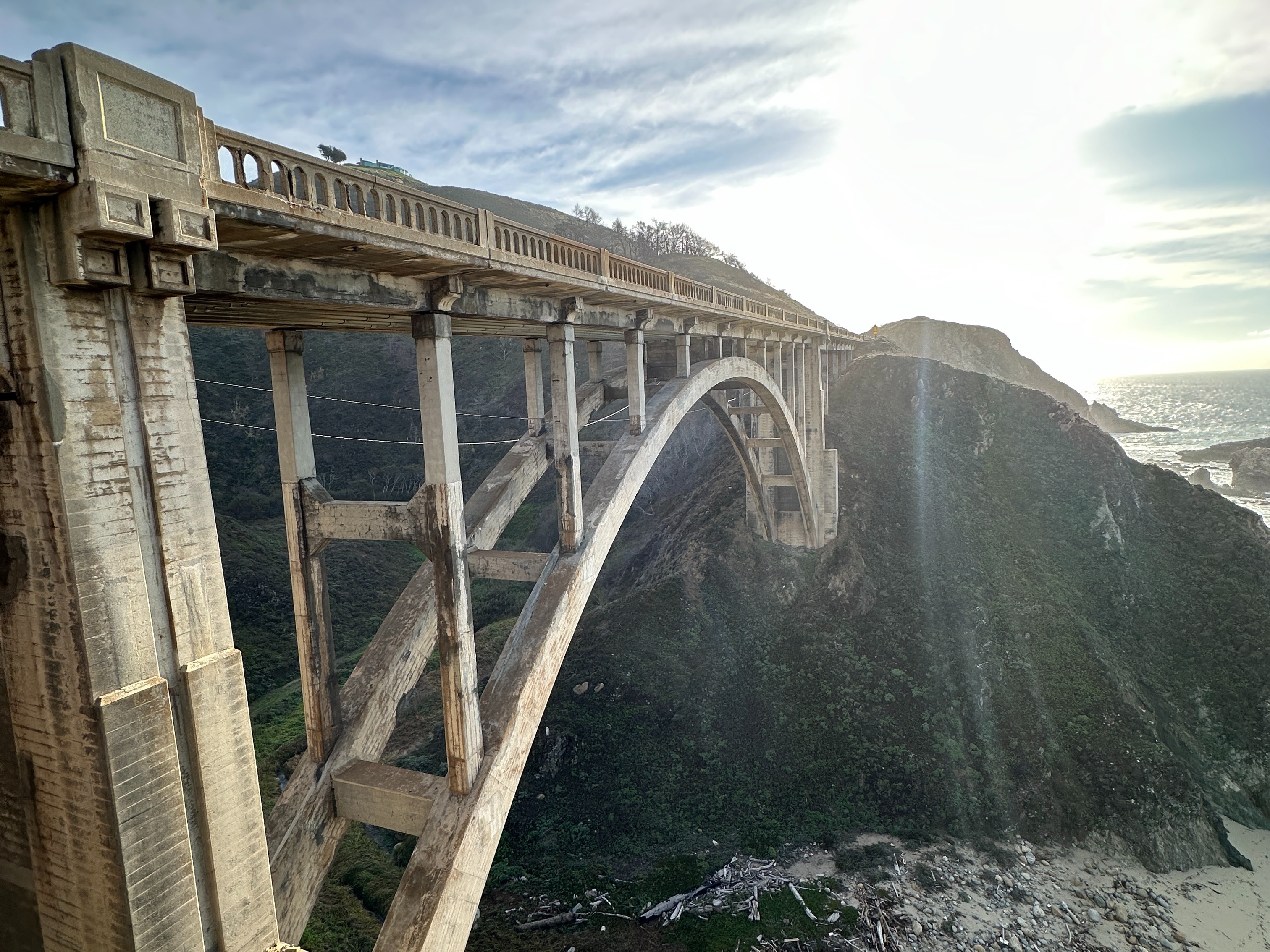 The image shows the iconic large concrete bridge with arches over a coastal landscape, illuminated by sunlight.