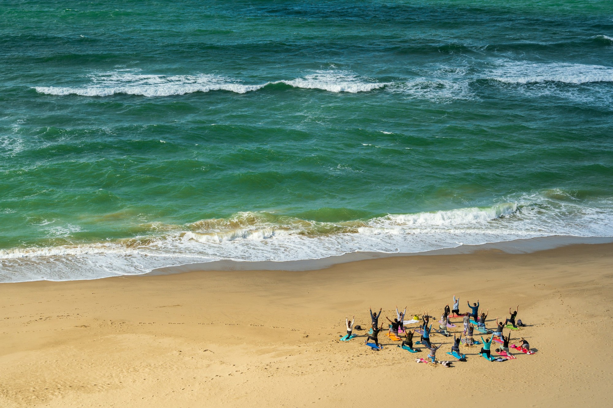 A group of people practicing yoga on the beach with the ocean behind them.