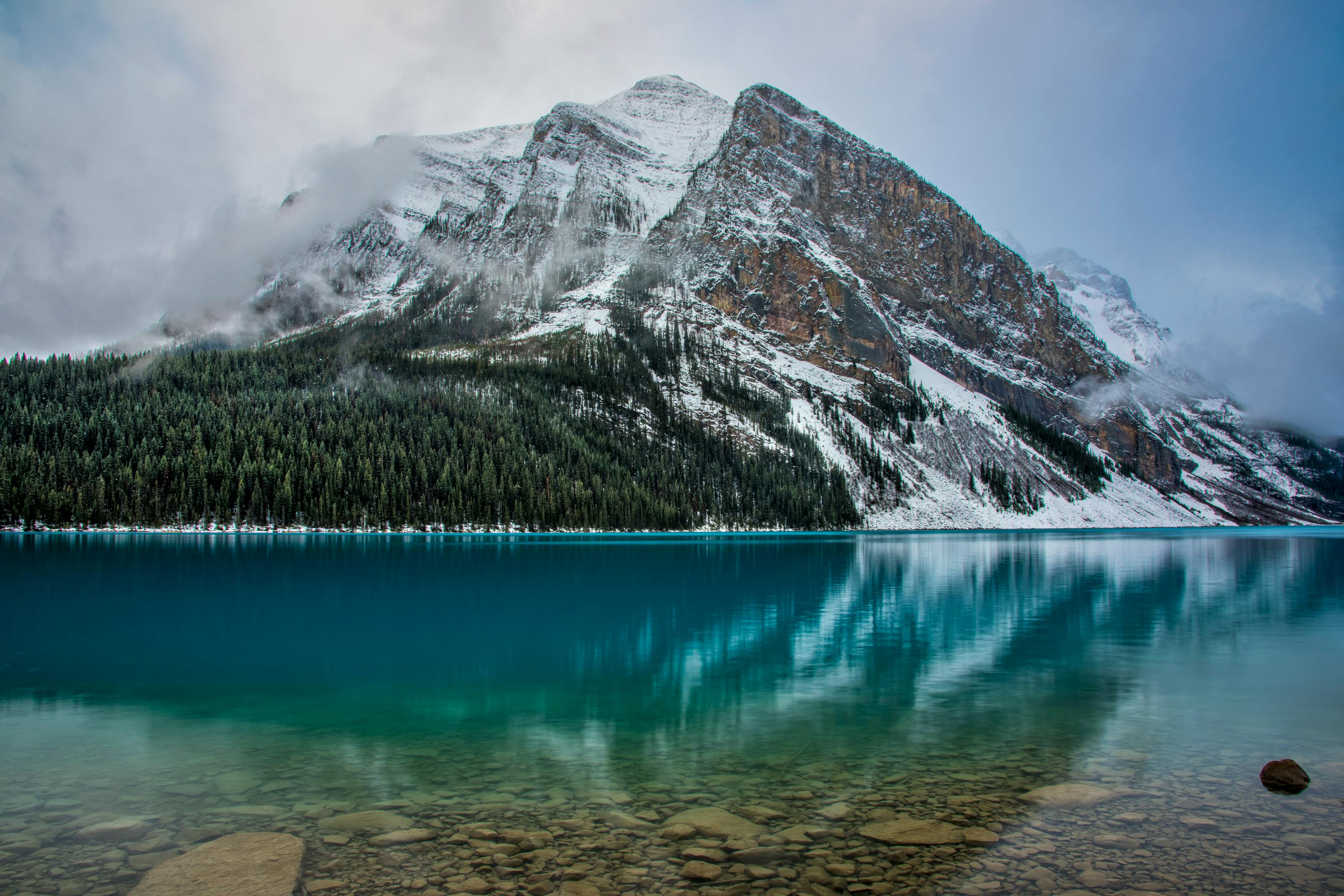 The serene Lake Louise in Banff National Park reflecting the mountainous range that stands tall against the misty sky.