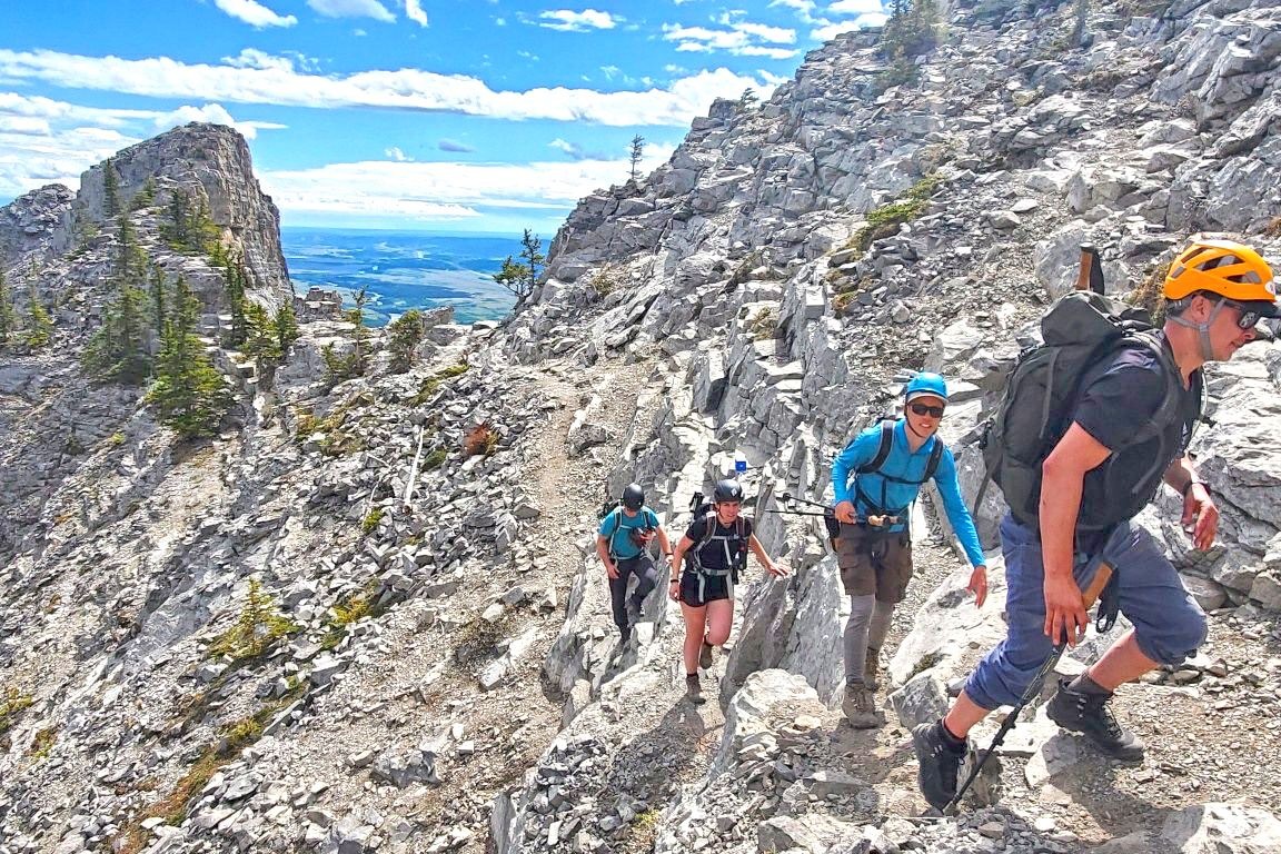 Experience mountaineering with Yamnuska Mountain Adventures as a tour treks up rocky terrain on a sunny day.
