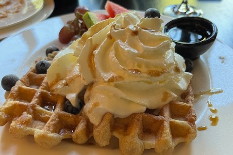 A waffle on a plate covered in fruit and whipped cream