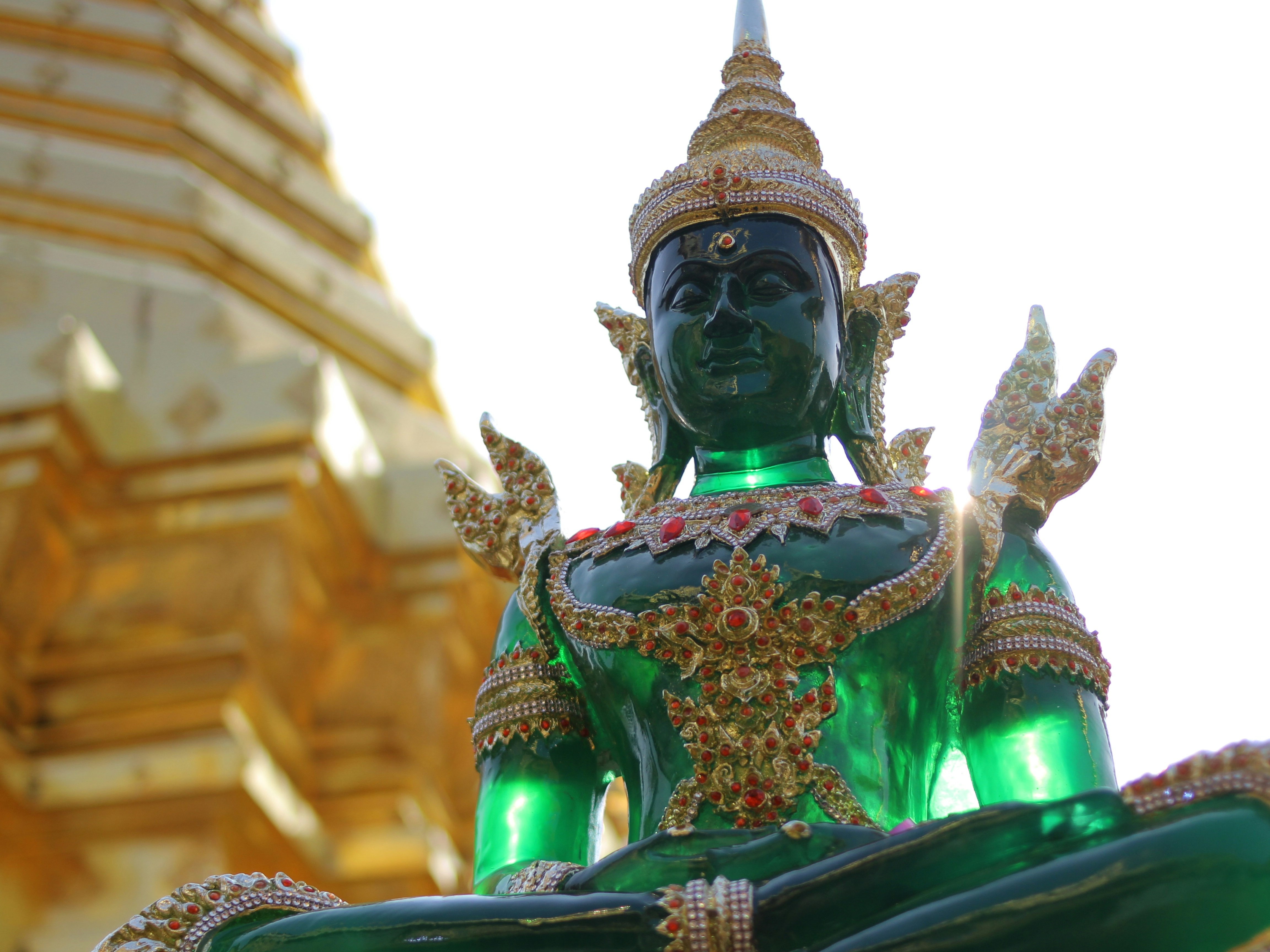 A green, ornately decorated statue stands in front of a golden structure, likely within a religious or cultural site.