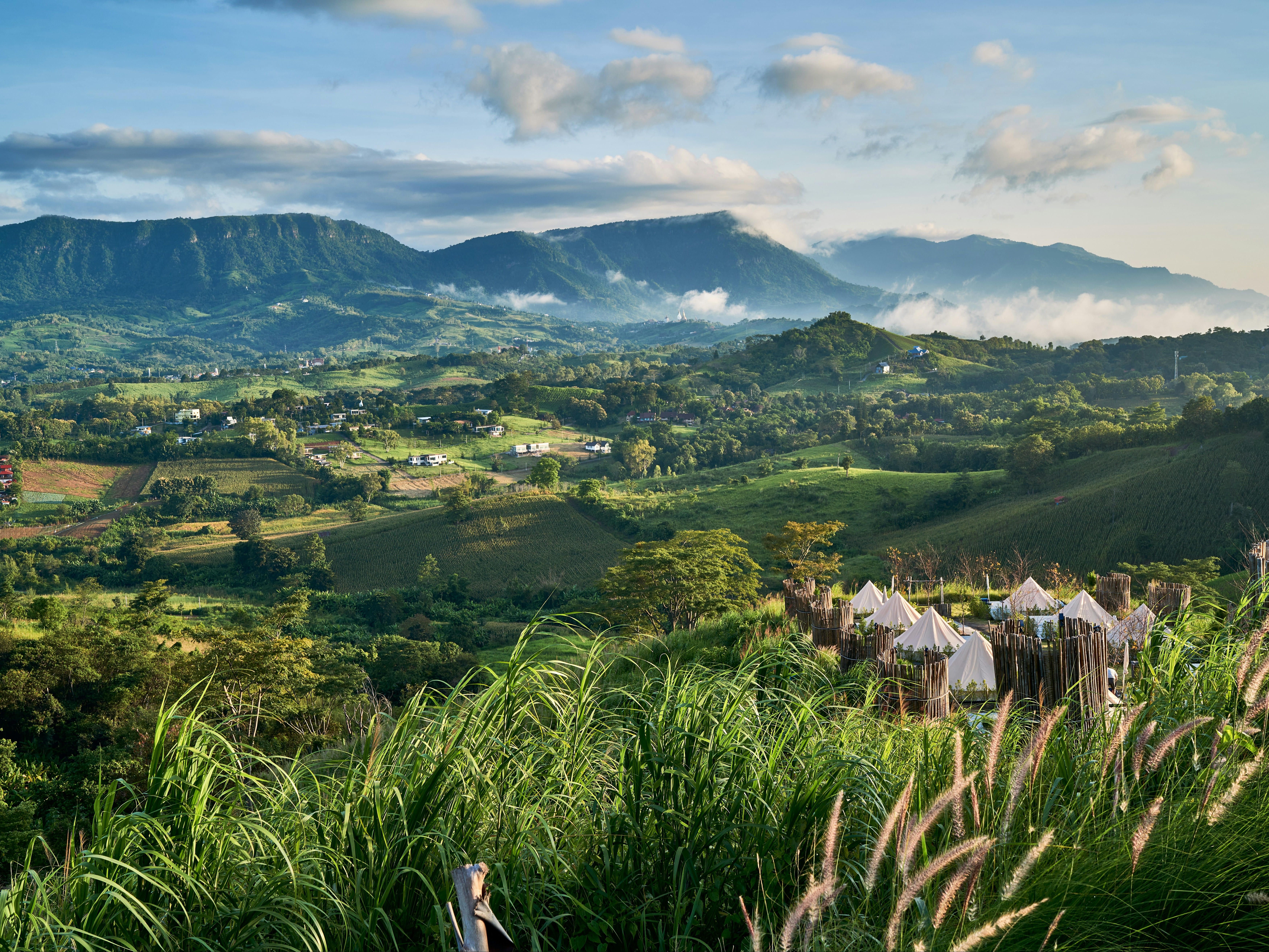 A lush, green landscape with mountains and a small settlement under low-hanging clouds.