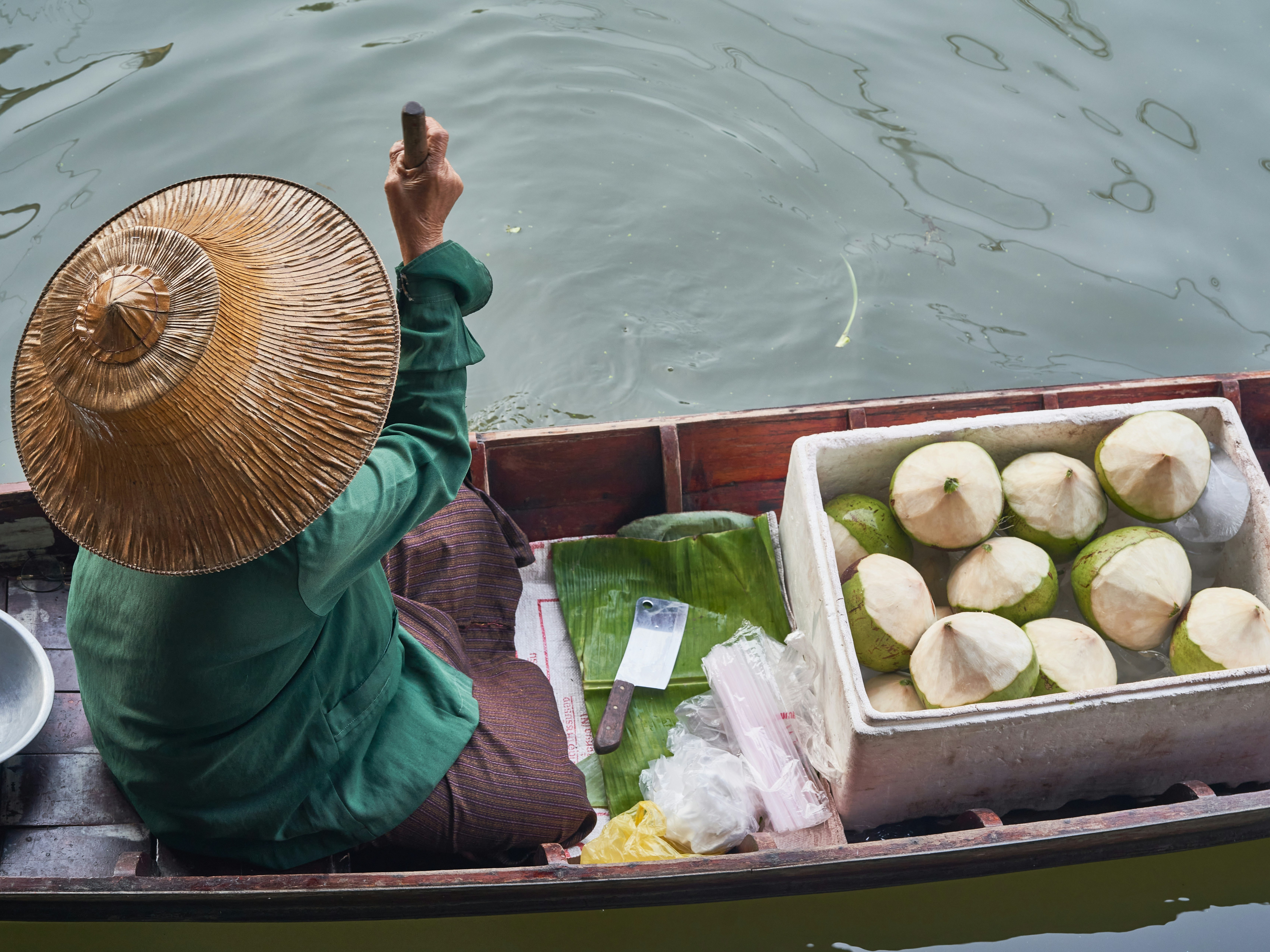 An individual in a boat is selling fresh coconuts at a floating market.