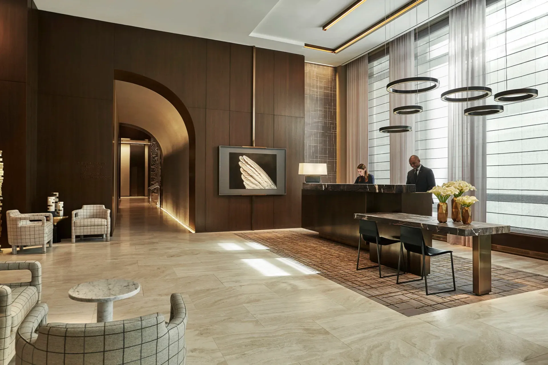 A classy lobby with abstract art and thoughtfully designed furniture, plus a reception desk with two staffers in formal dress