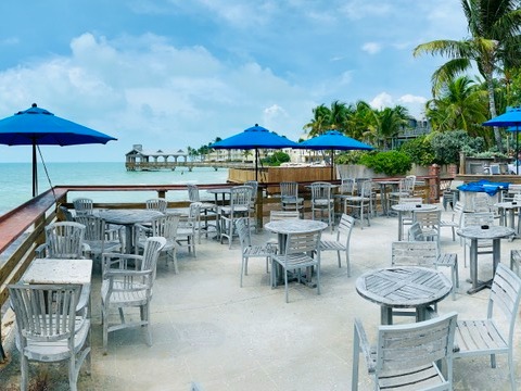 The image shows a beachfront with multiple colorful umbrellas, outdoor seating, and a clear sky, suggesting a leisure or vacation setting.