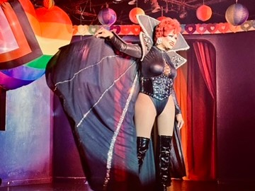 The image shows a performer on stage with a large fabric prop, surrounded by colorful lighting and decorations.