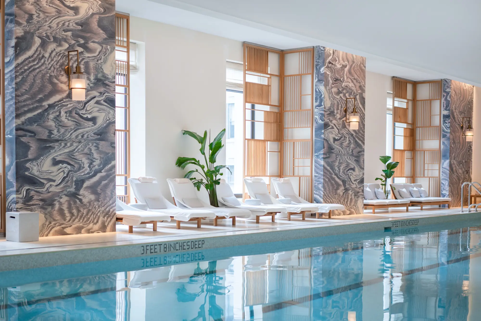 large indoor pool surrounded by white loungers and potted plants, plus views of the city skyline