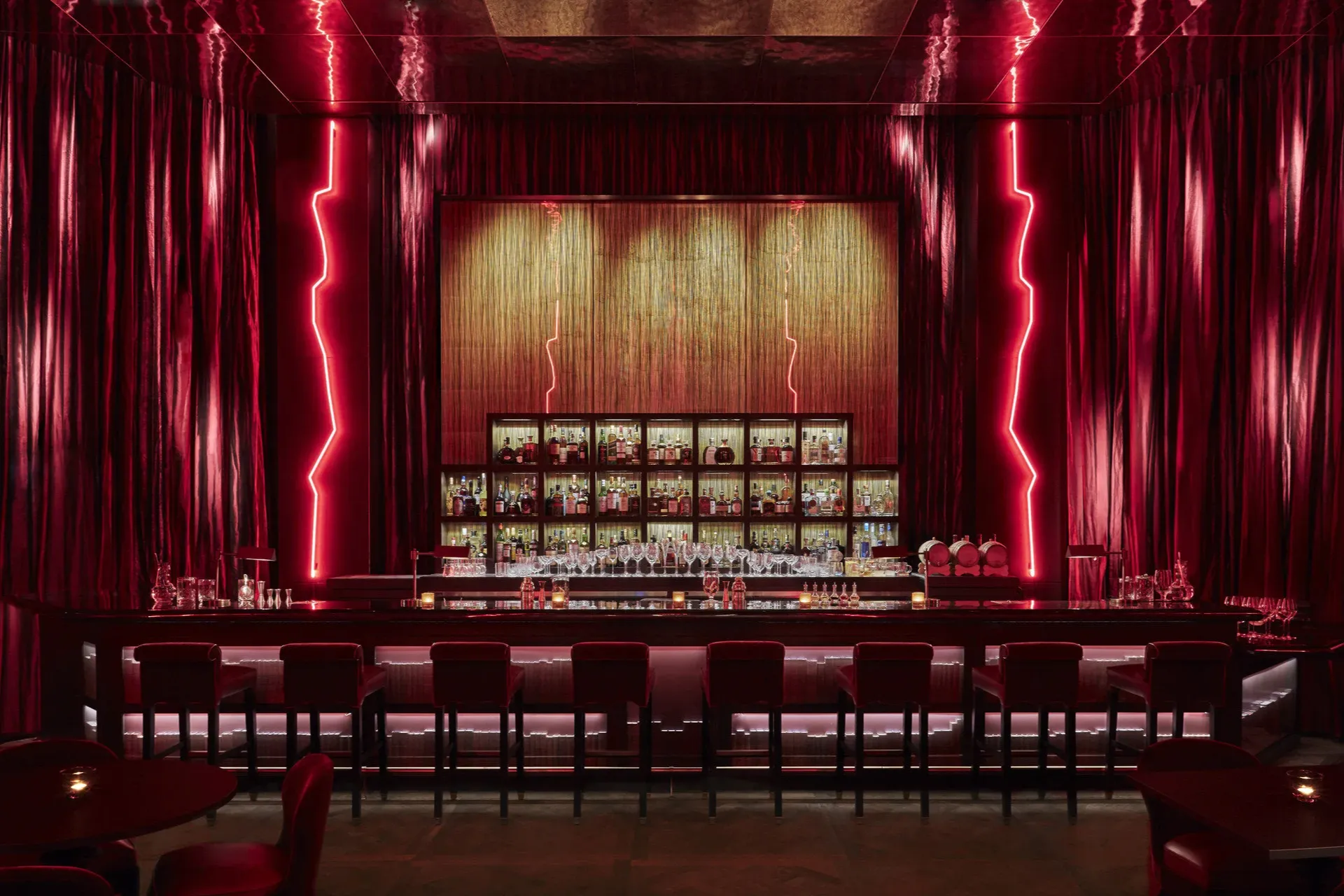Classy long bar with top-shelf options, red neon lighting rising like lightning bolts out of the ground and velvet drapes lining the wals