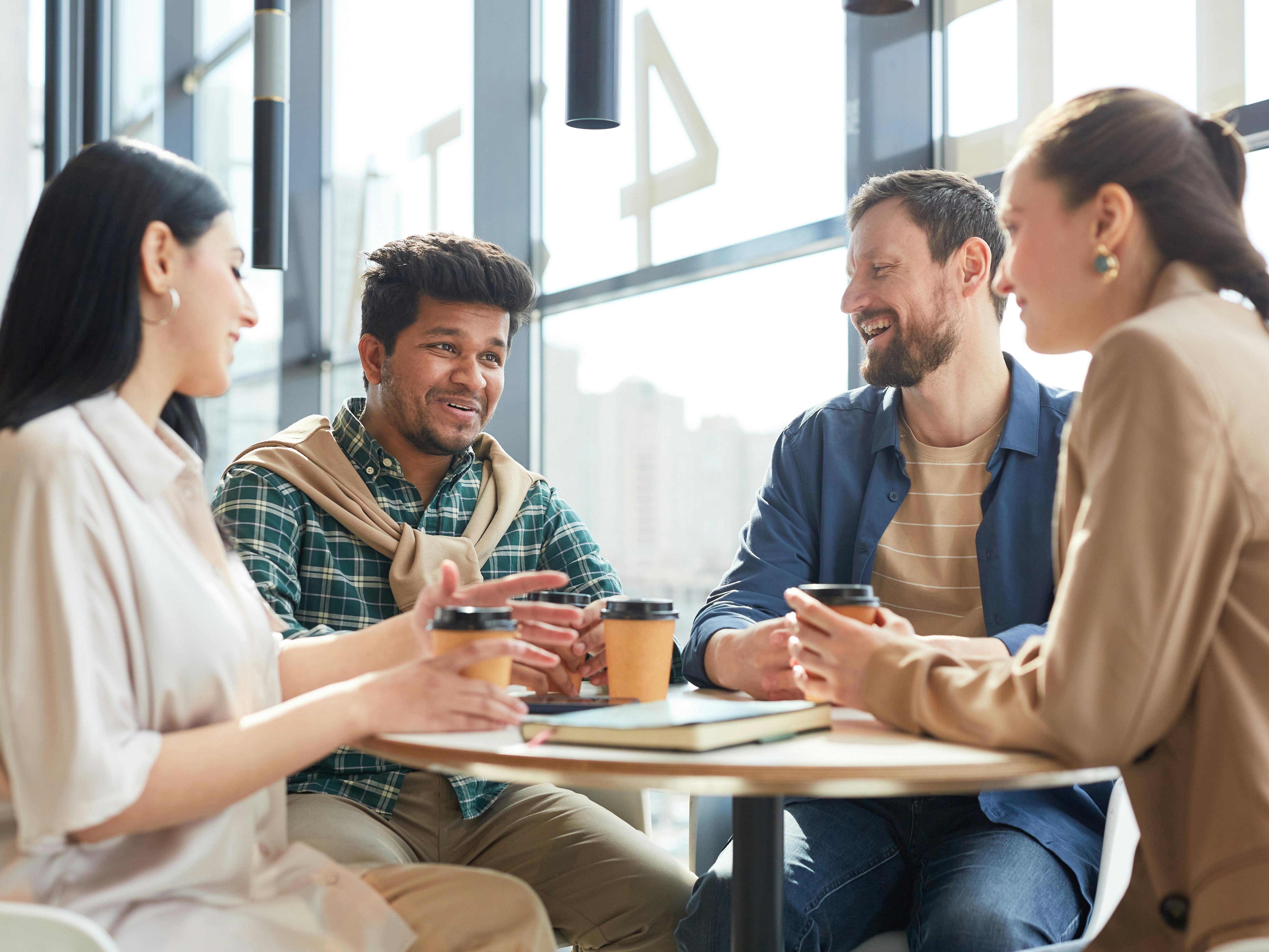 Four individuals sit around a table in a discussion at a cafe on a sunny day.