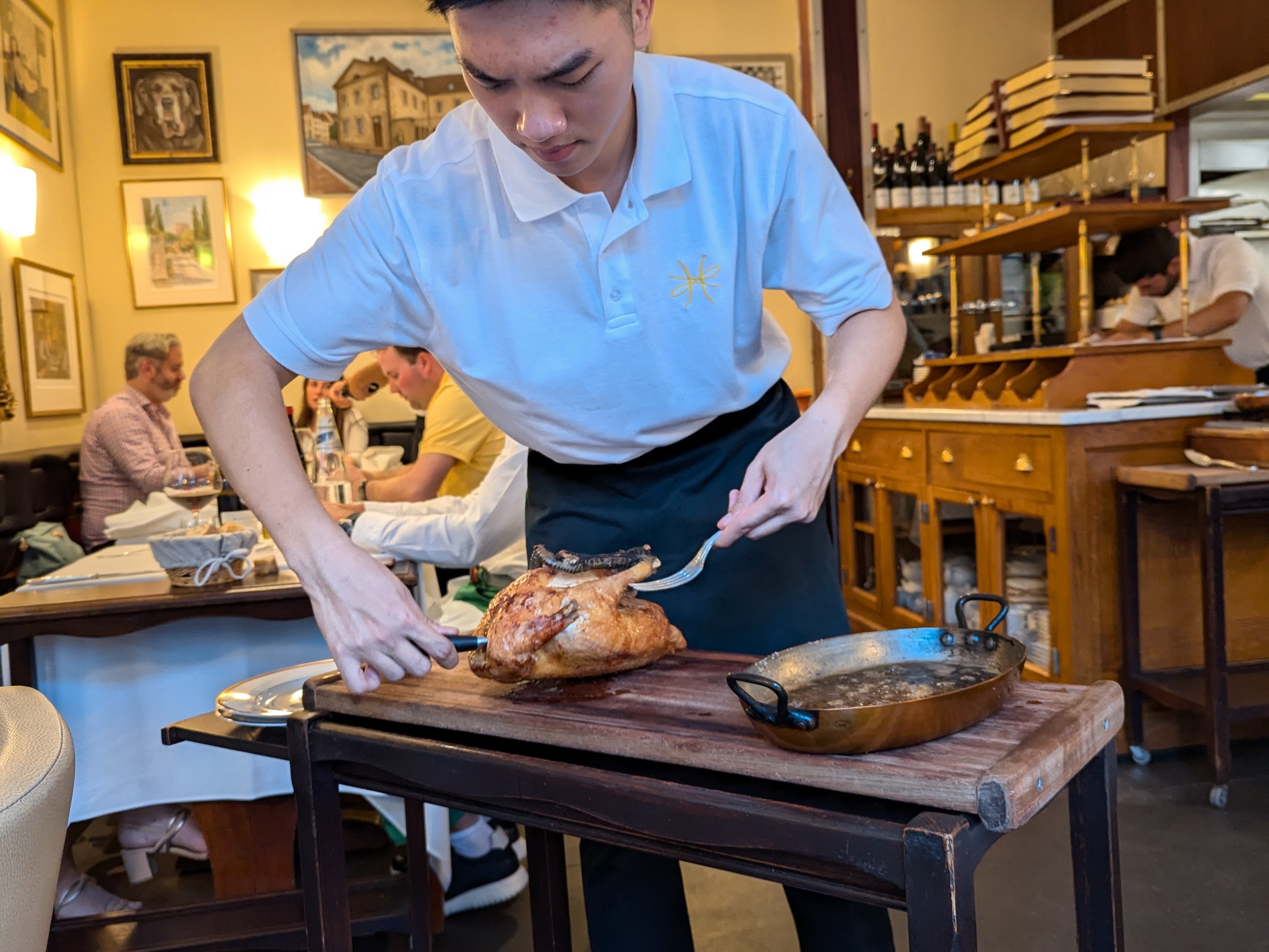 A person carving a roasted chicken on a wooden board in a restaurant setting.