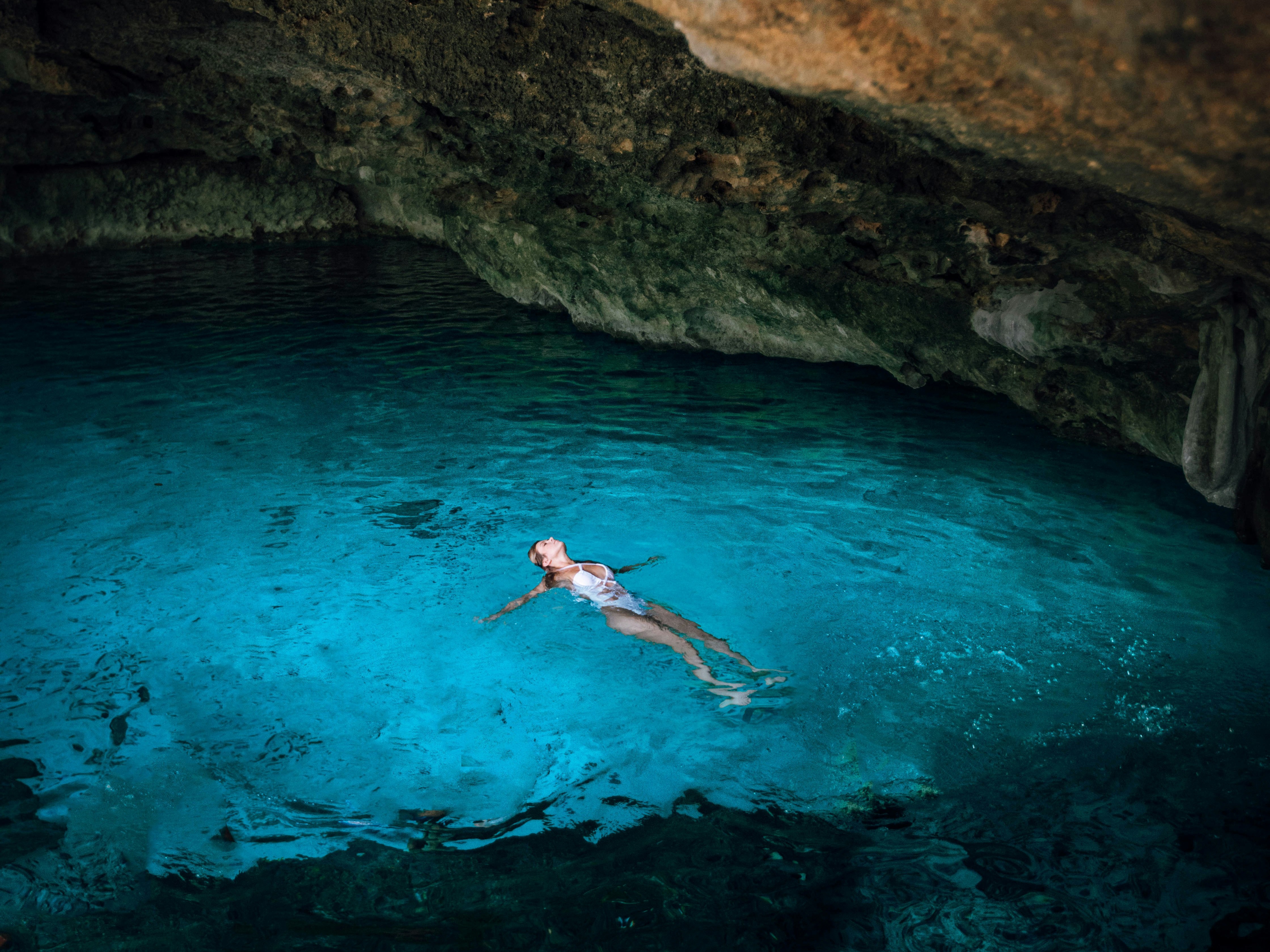 A person swimming in clear blue water under a rocky cave, creating a serene underwater scene.