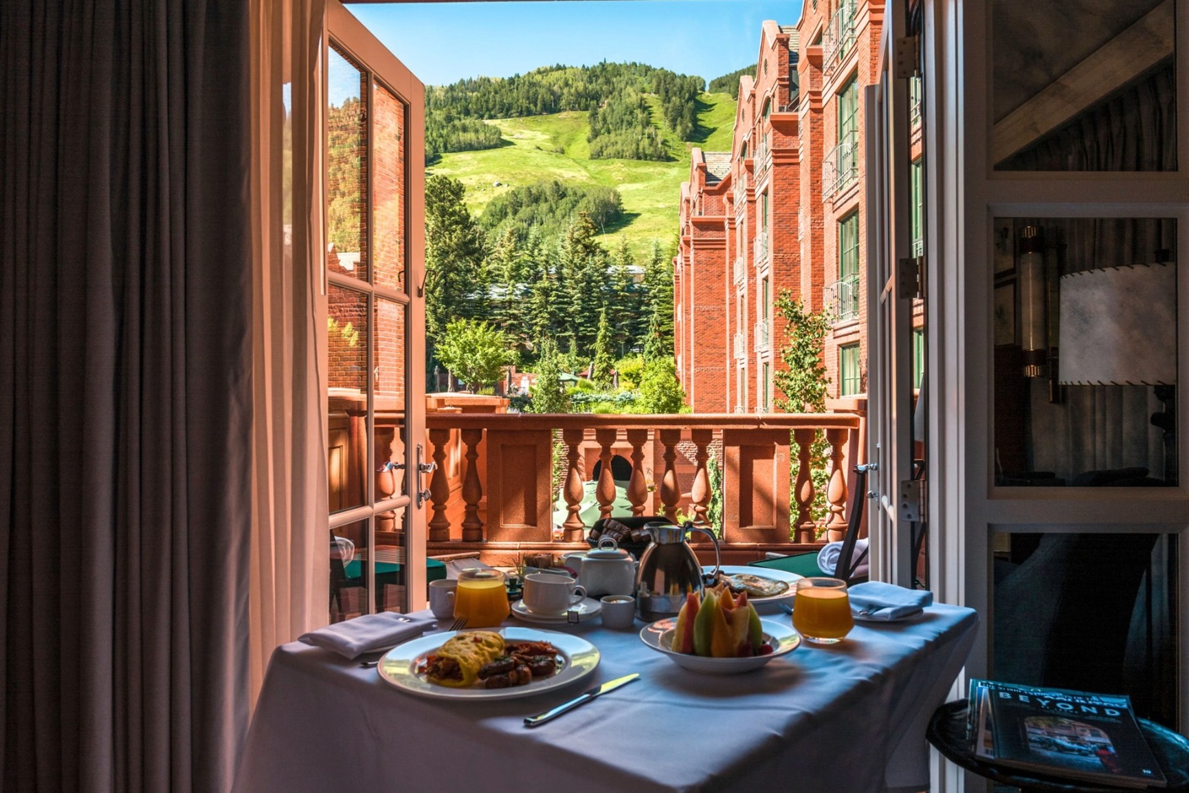 view of a green mountain from a room with open glass doors and a room service table of food