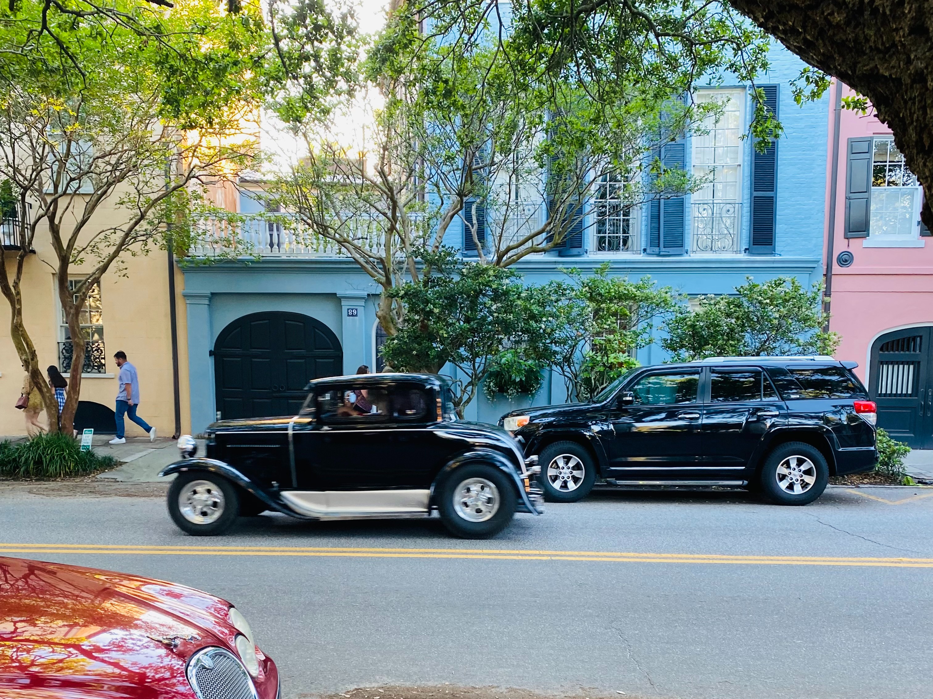 A street view with a vintage car parked between two modern vehicles highlights a contrast in automotive history.