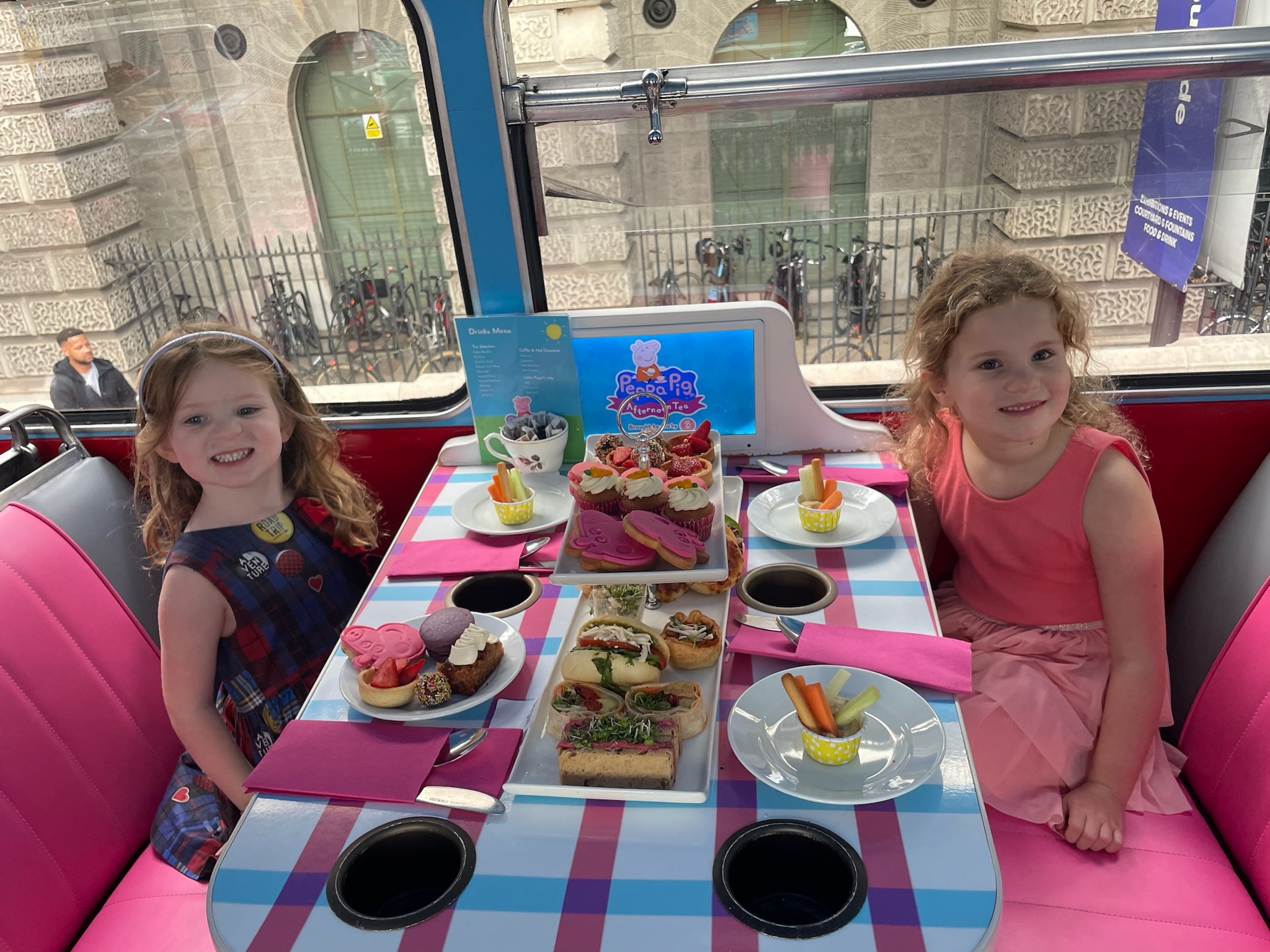 Two children sitting at a table inside a vehicle, enjoying an array of colorful desserts and snacks.