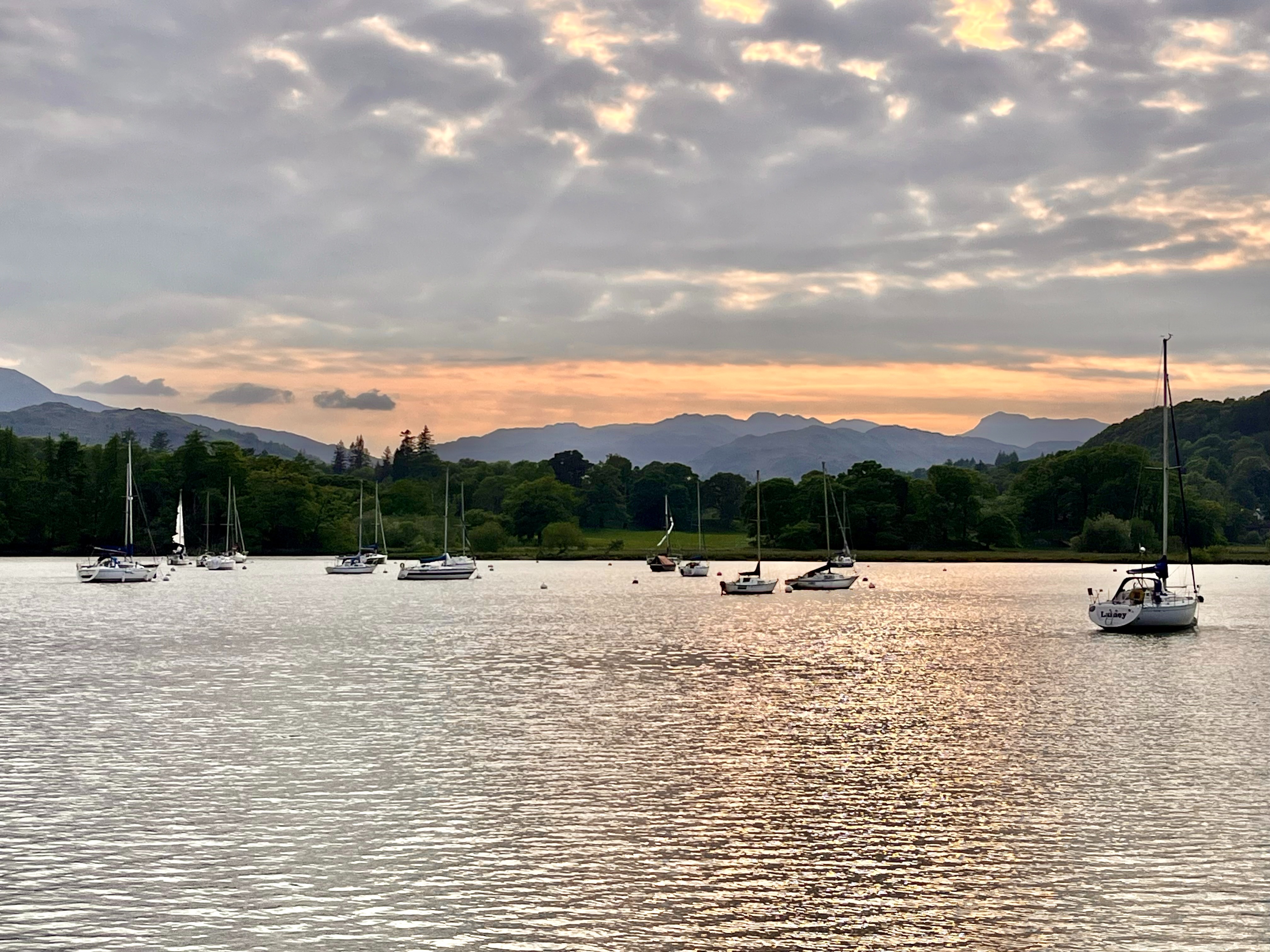 The image shows a lake with multiple sailboats at sunset, reflecting the sunset on a cloudy day