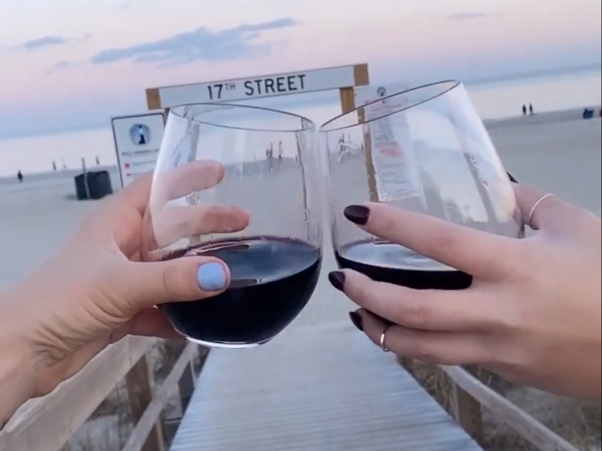 Two wine glasses being toasted on a beach at dusk.