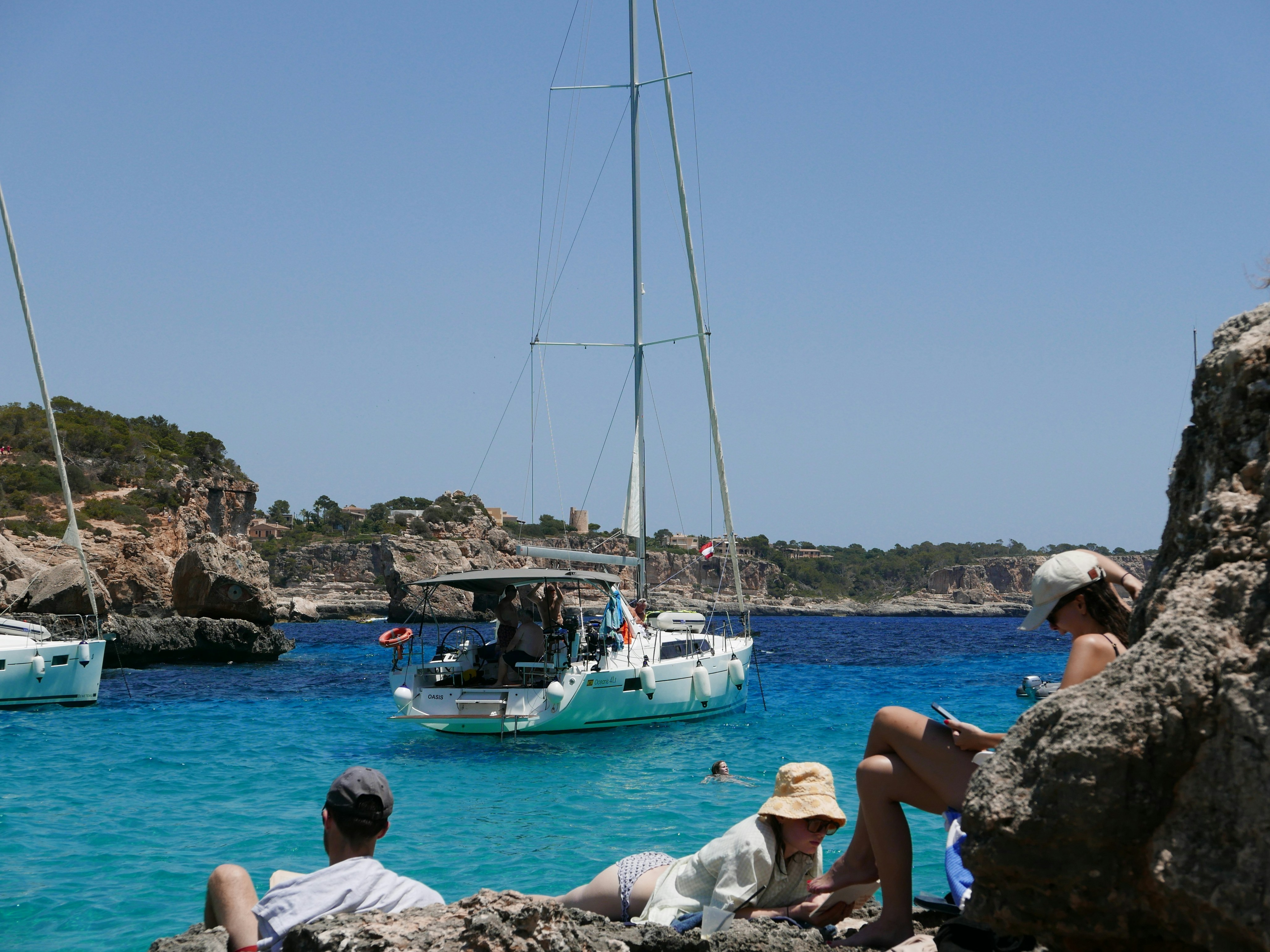 people-sitting-on-rocks-looking-at-a-sailboat-mallorca-travel-guide