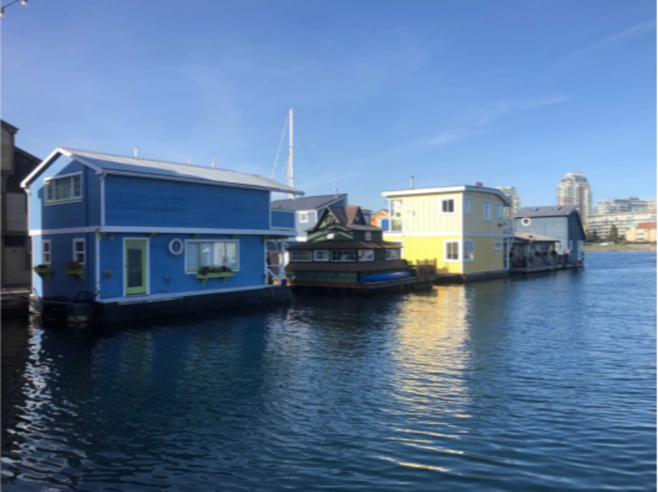 The image shows colorful floating houses on calm water under clear skies, anchored along a dock.