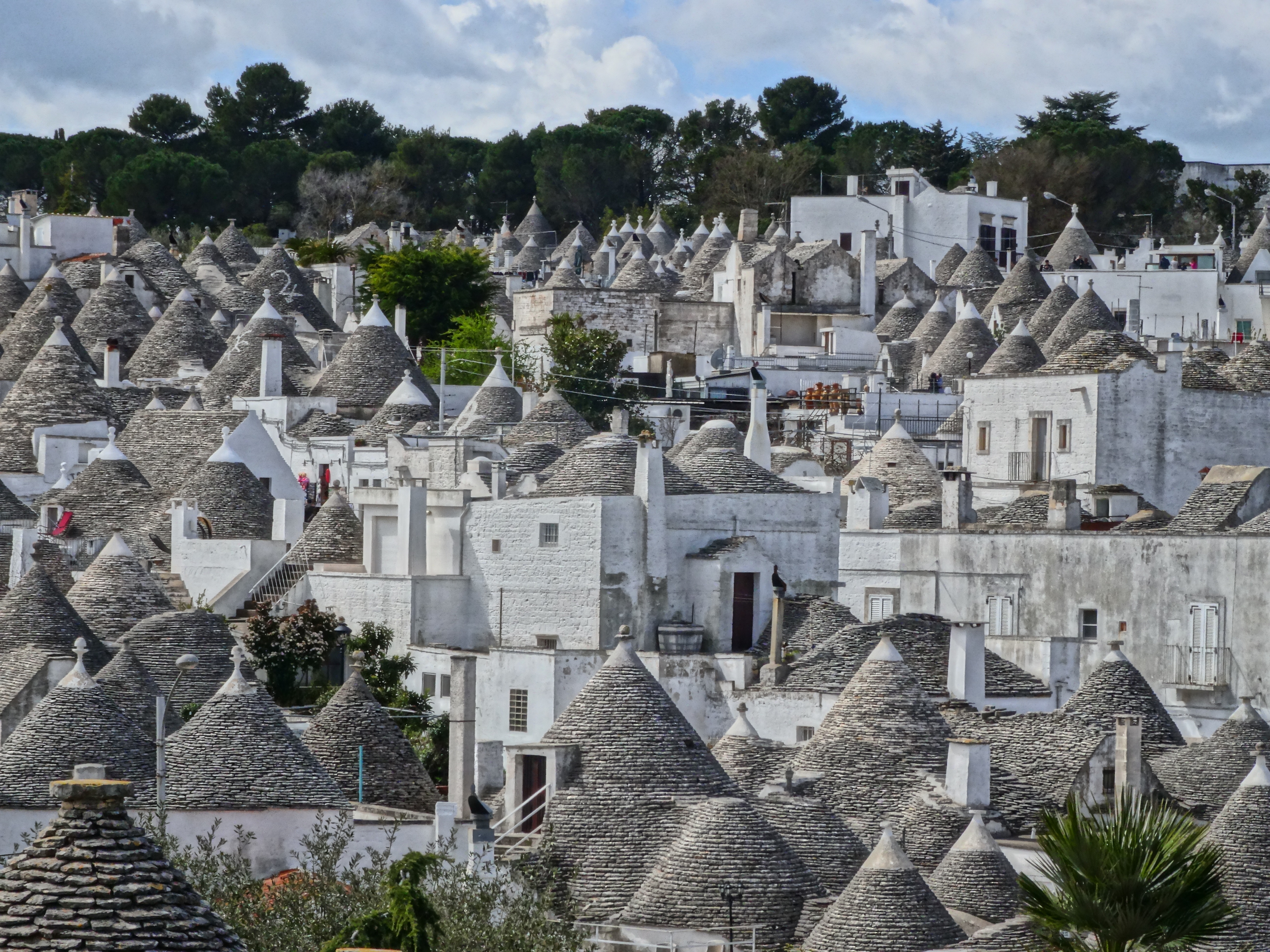A dense cluster of traditional trulli houses with conical roofs under a cloudy sky.