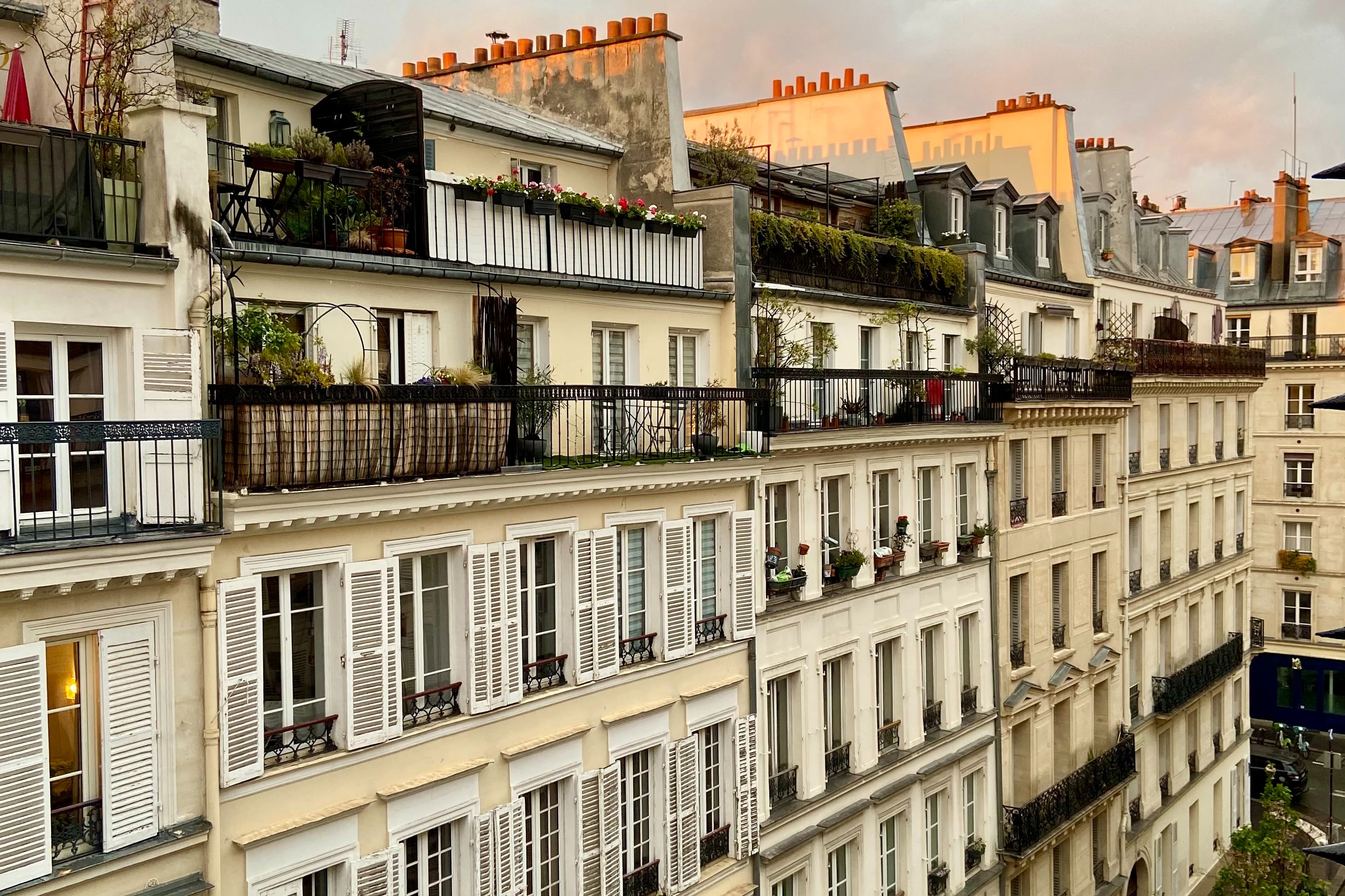 View of Parisian apartments with balconies from a side angle against a soft sky at dusk.