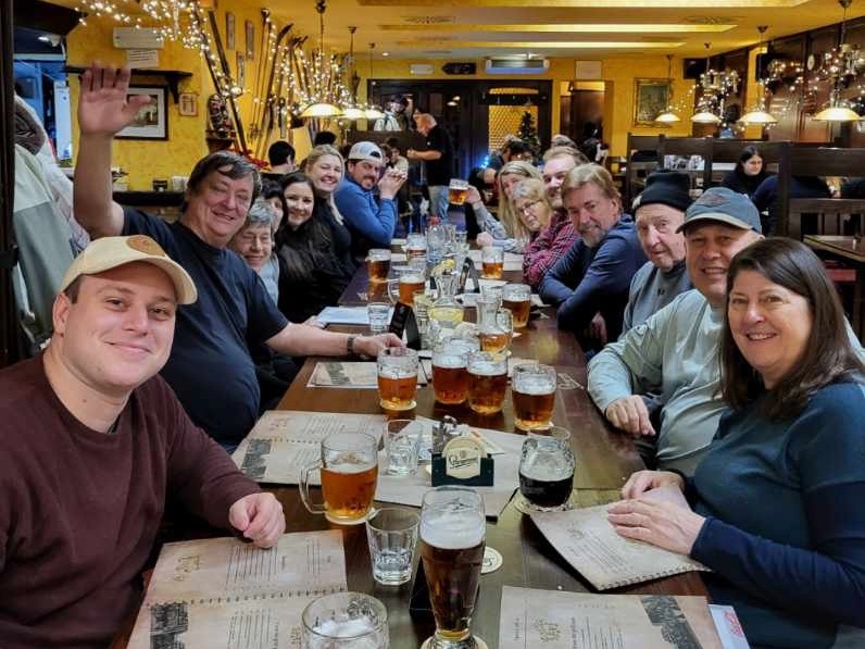 A group of individuals seated at a table in a pub or restaurant, engaging in social interaction with beers and menus.