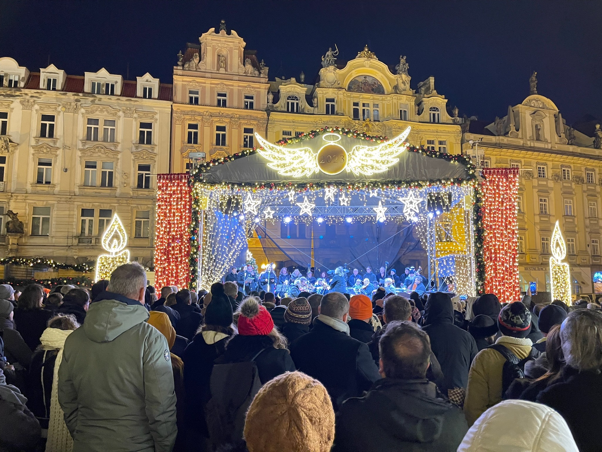 A crowd of people watching a live performance on an ornately decorated stage with festive lights.