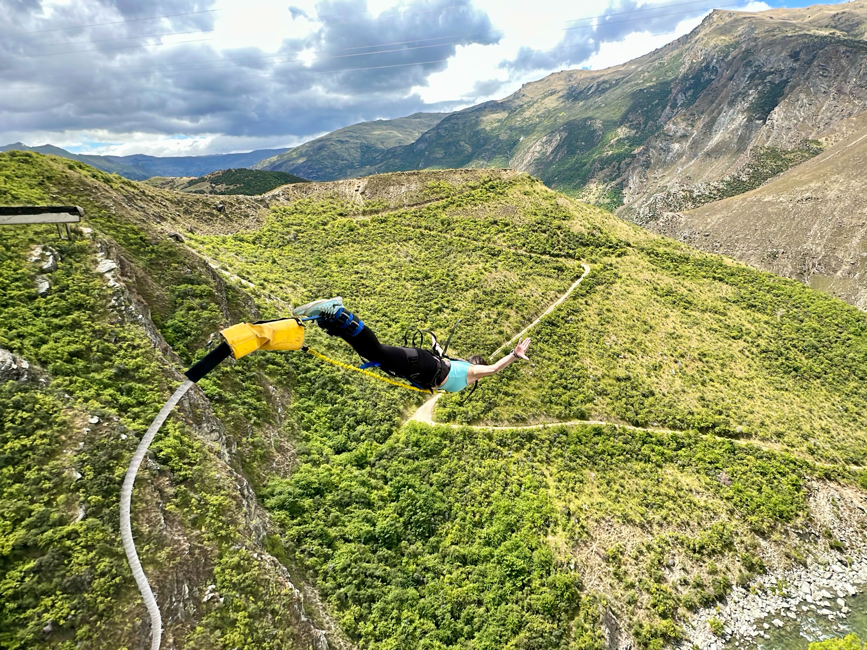 A person bungee jumping from a platform over a green valley with mountains in the background.