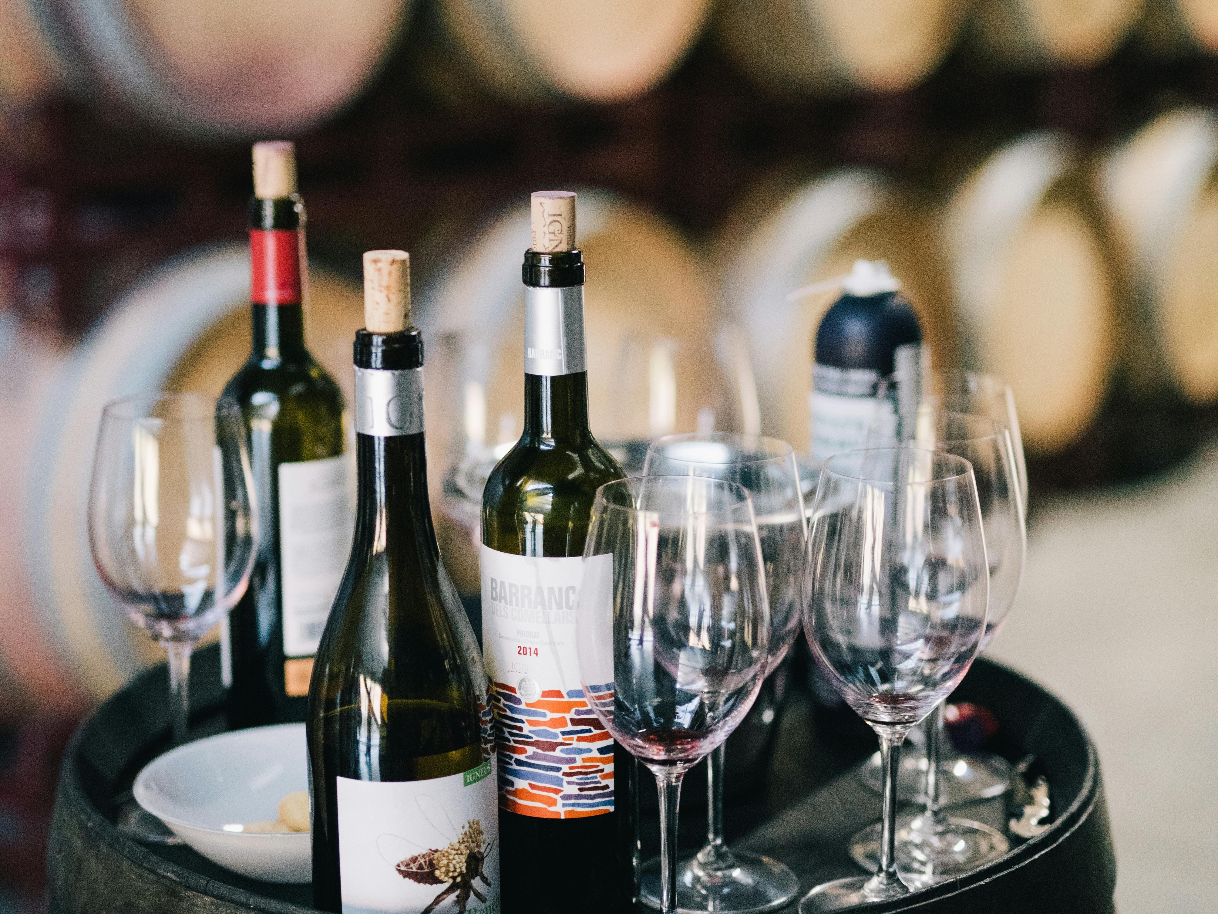 A selection of wine bottles and glasses arranged on top of a wooden barrel, suggests a wine-tasting setting.