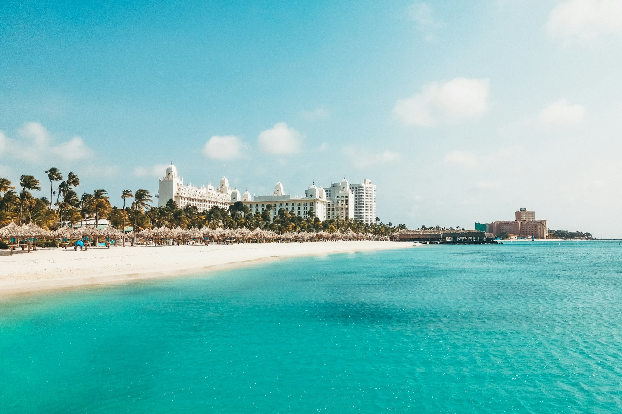 A view of the beach and bright blue water with hotel buildings in the distance