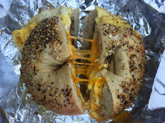 A bagel with melted cheese and eggs on aluminum foil.