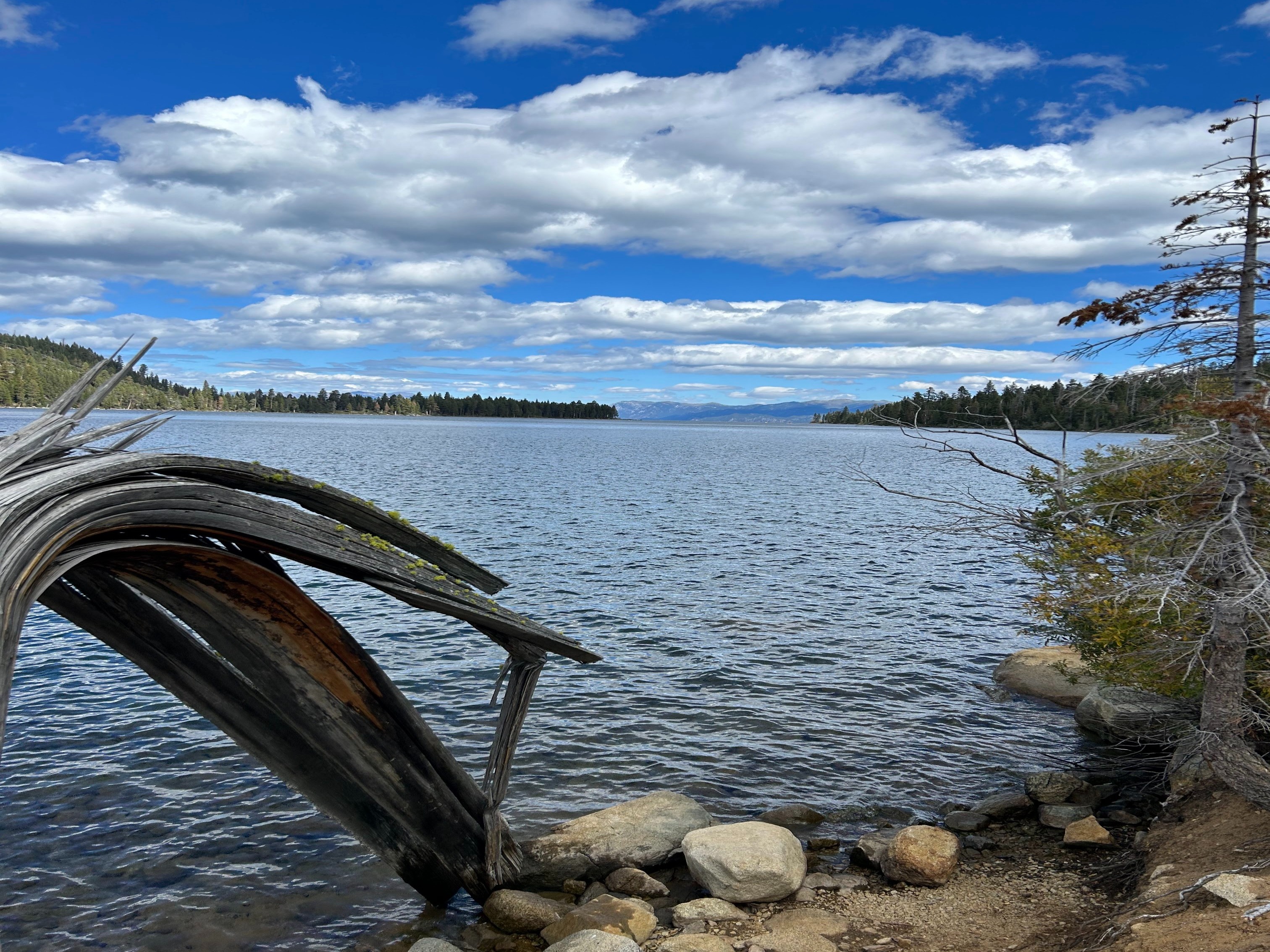 Rocks and trees surround a scenic lake with clear blue water under a partly cloudy sky.