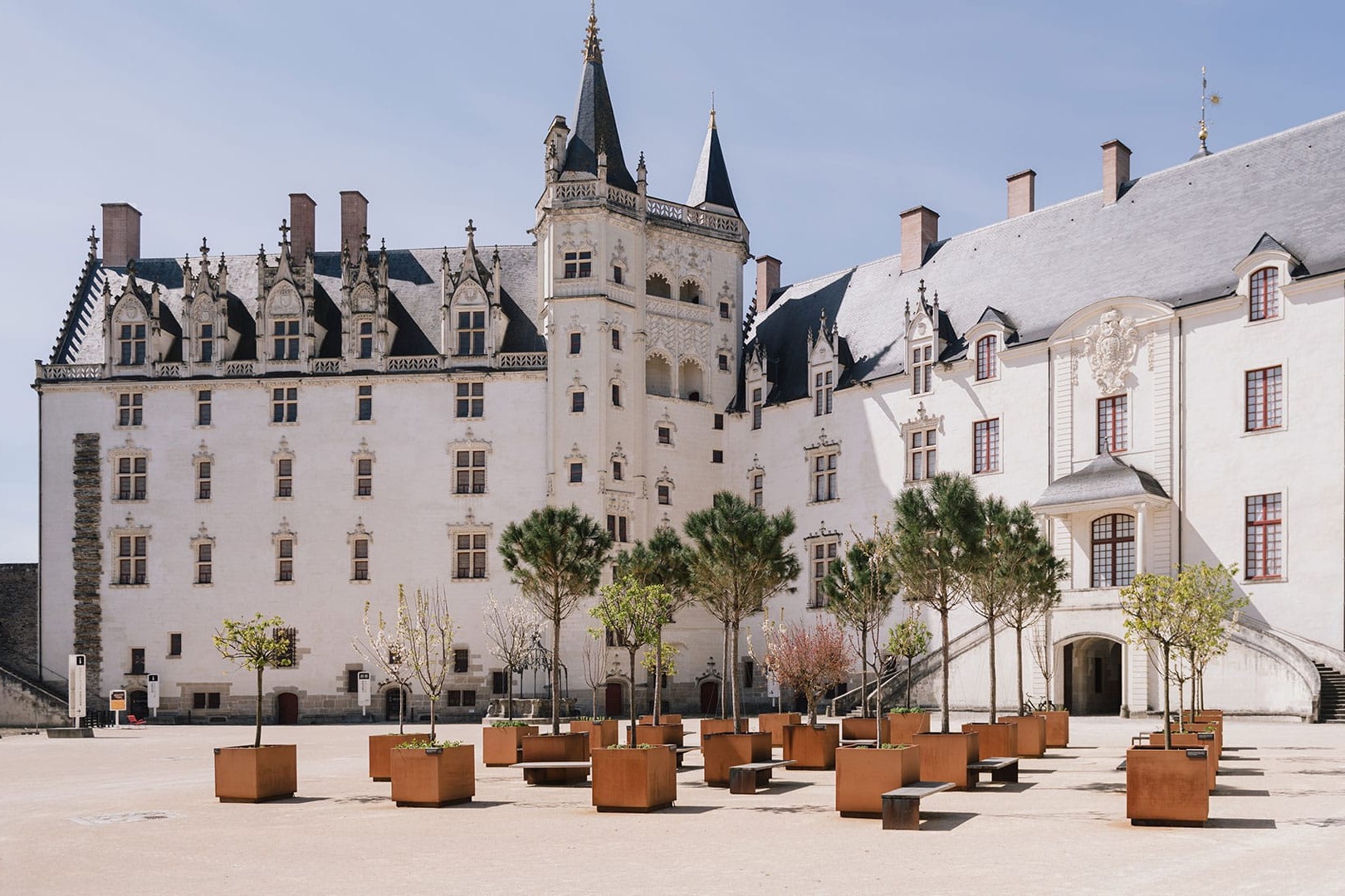 The image depicts a large white castle with a black roof and potted trees in the foreground at the Castle of the dukes of Brittany in Nantes, France
