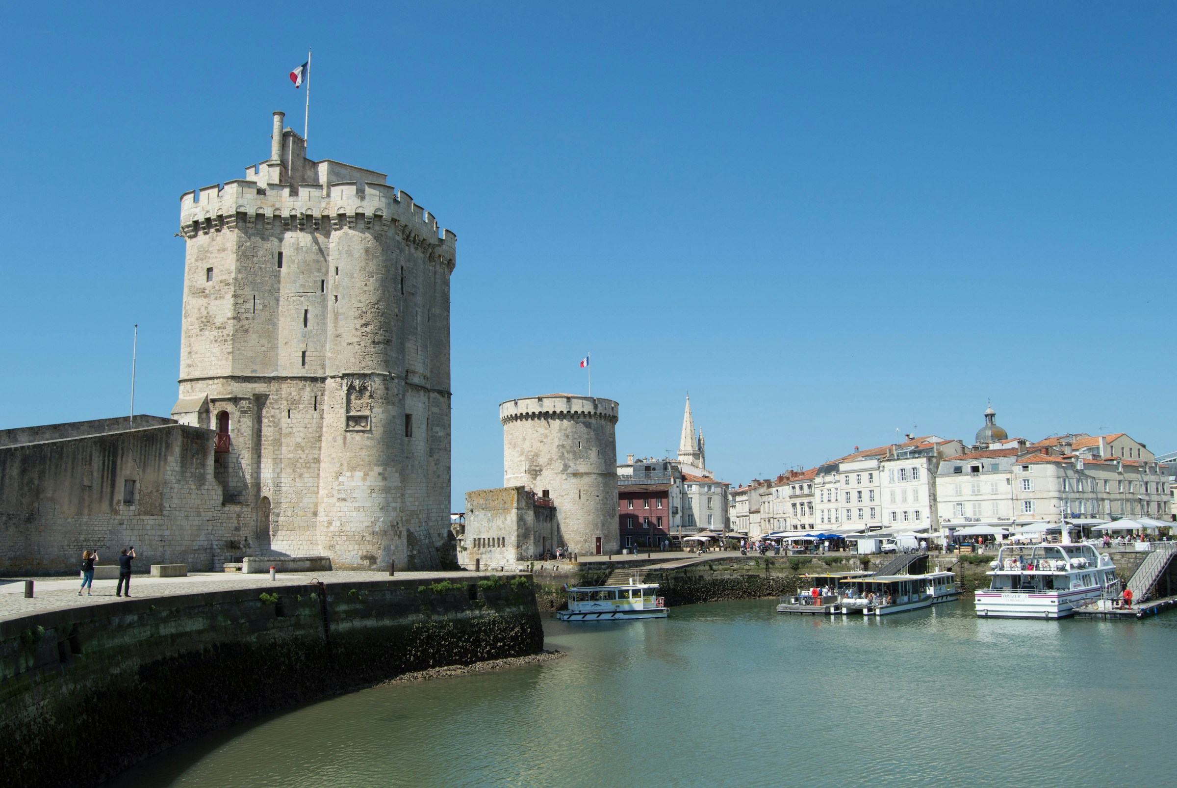 A view of a port with boats docked, a large stone castle and white buildings at the Vieux-Port which is the oldest port of La Rochelle.