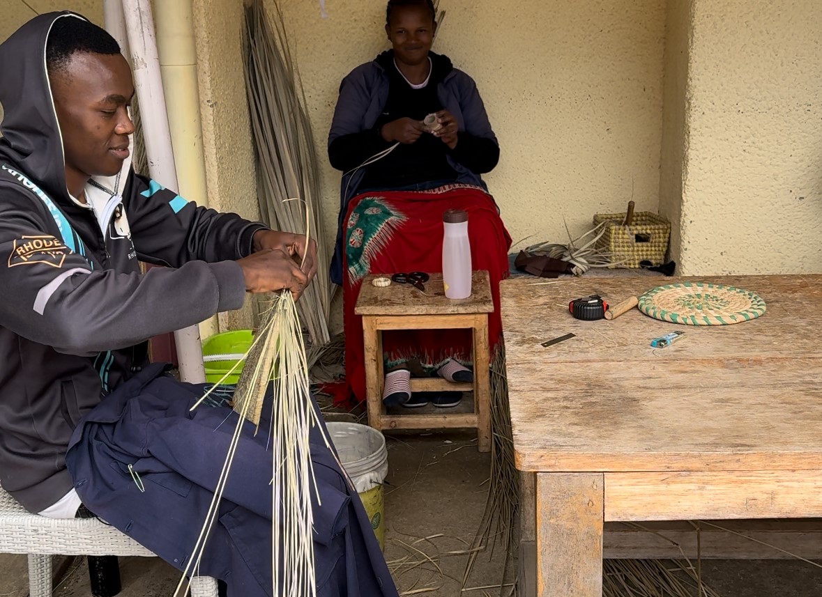 Two men sitting making items out of palm leaves.