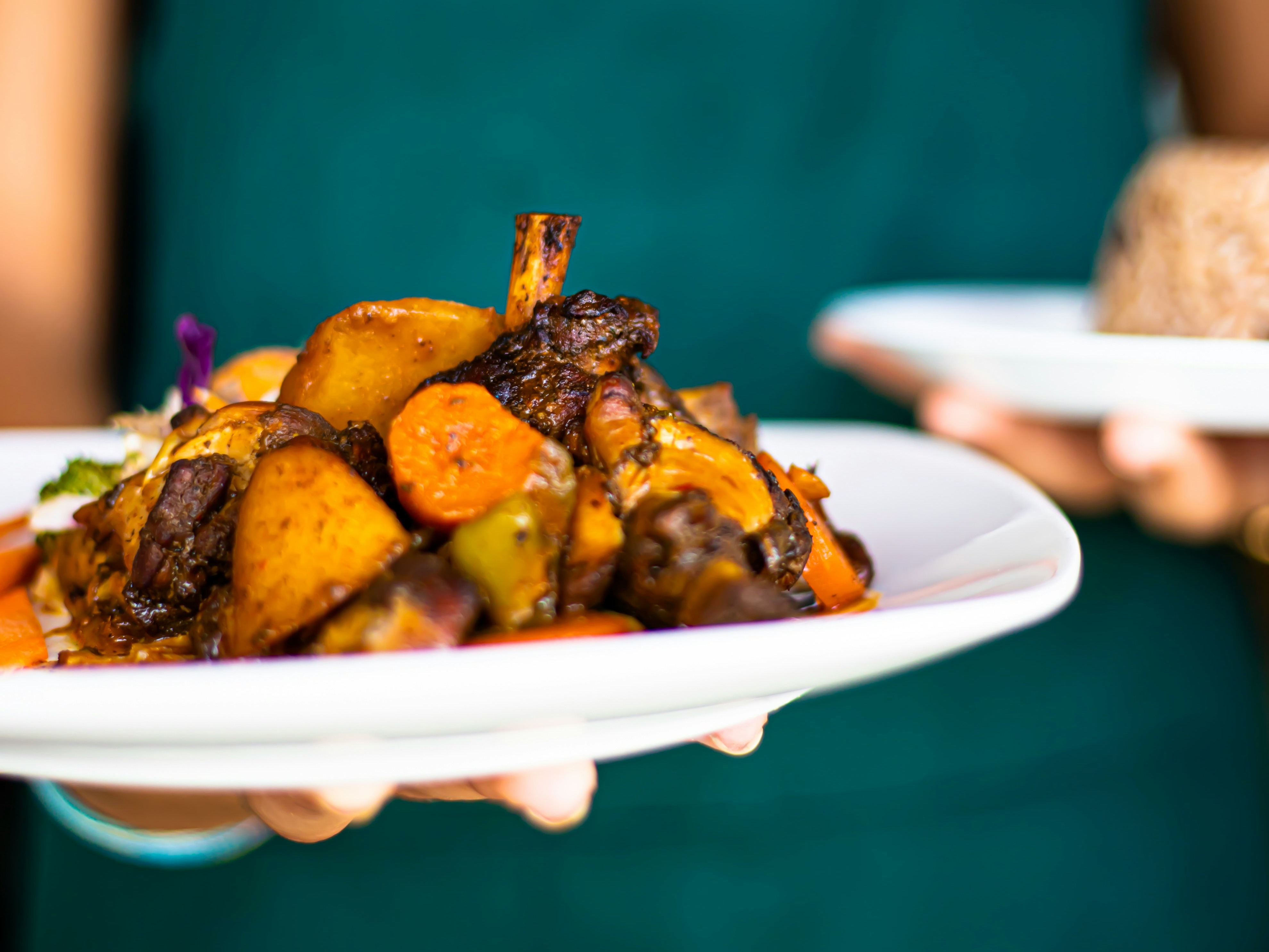A person in a green apron holding a plate of roasted vegetables and chicken