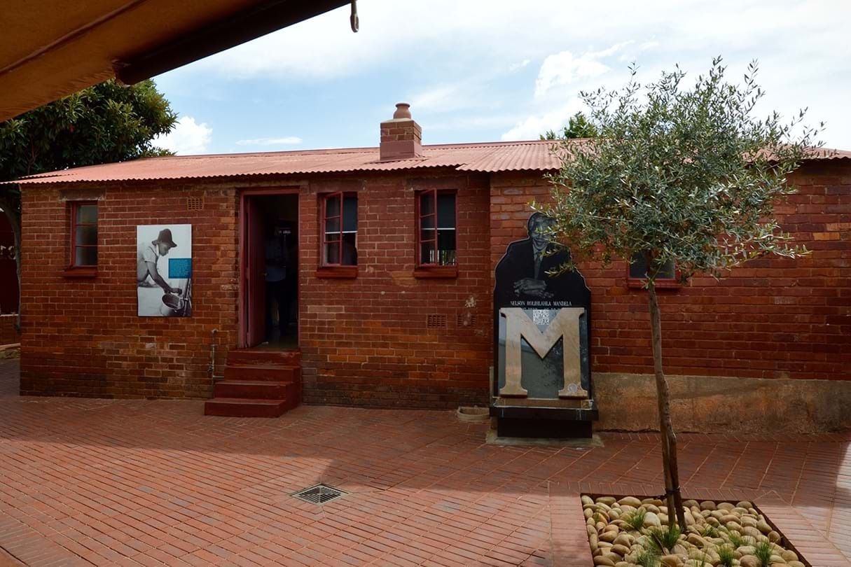 A small red brick building, with a large "M" and photo of Nelson Mandela on the outside. The Mandela House, the former residence of Nelson Mandela, showcasing his life and legacy.