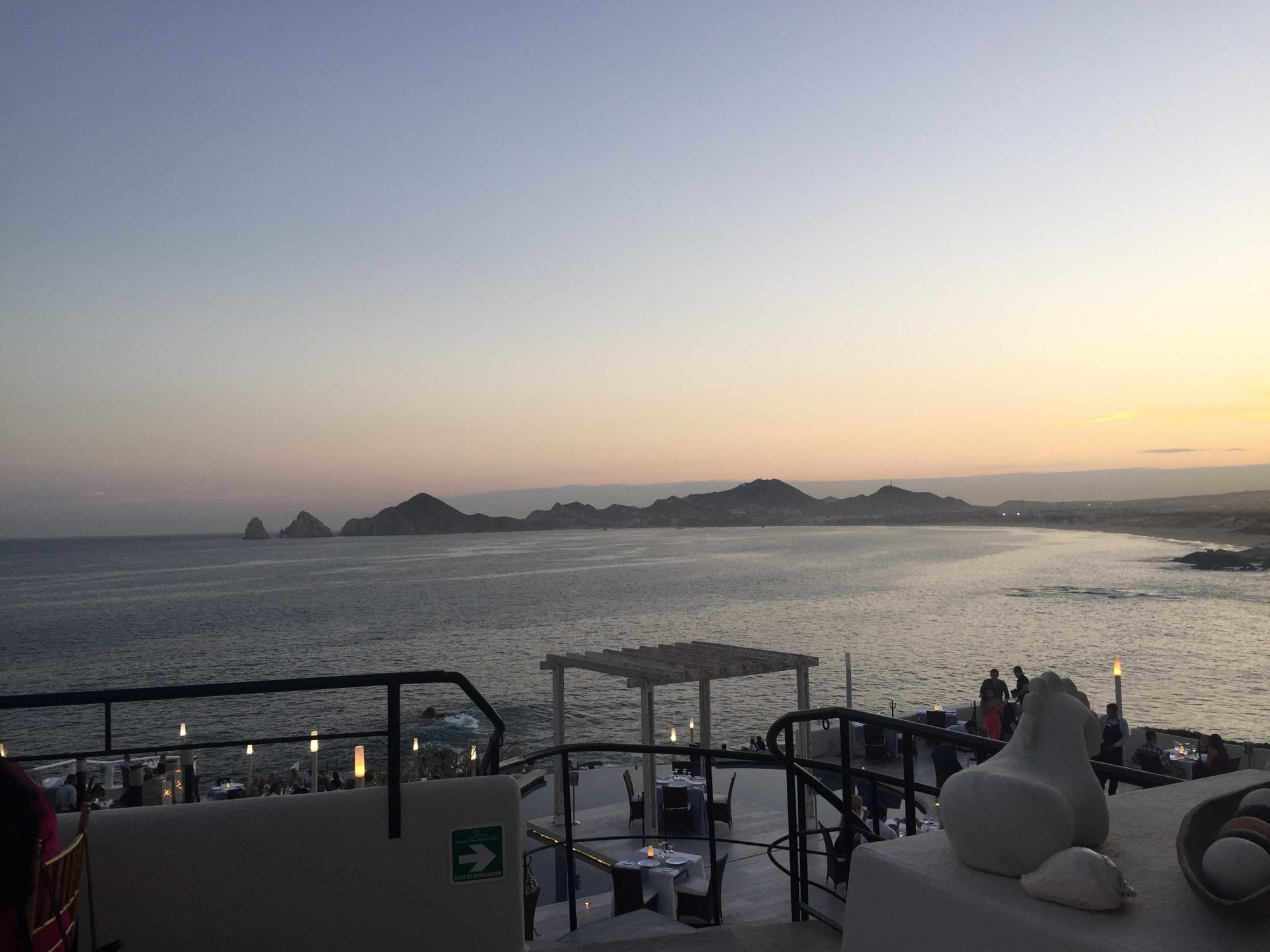 An outdoor seating area looking out onto the water at sunset