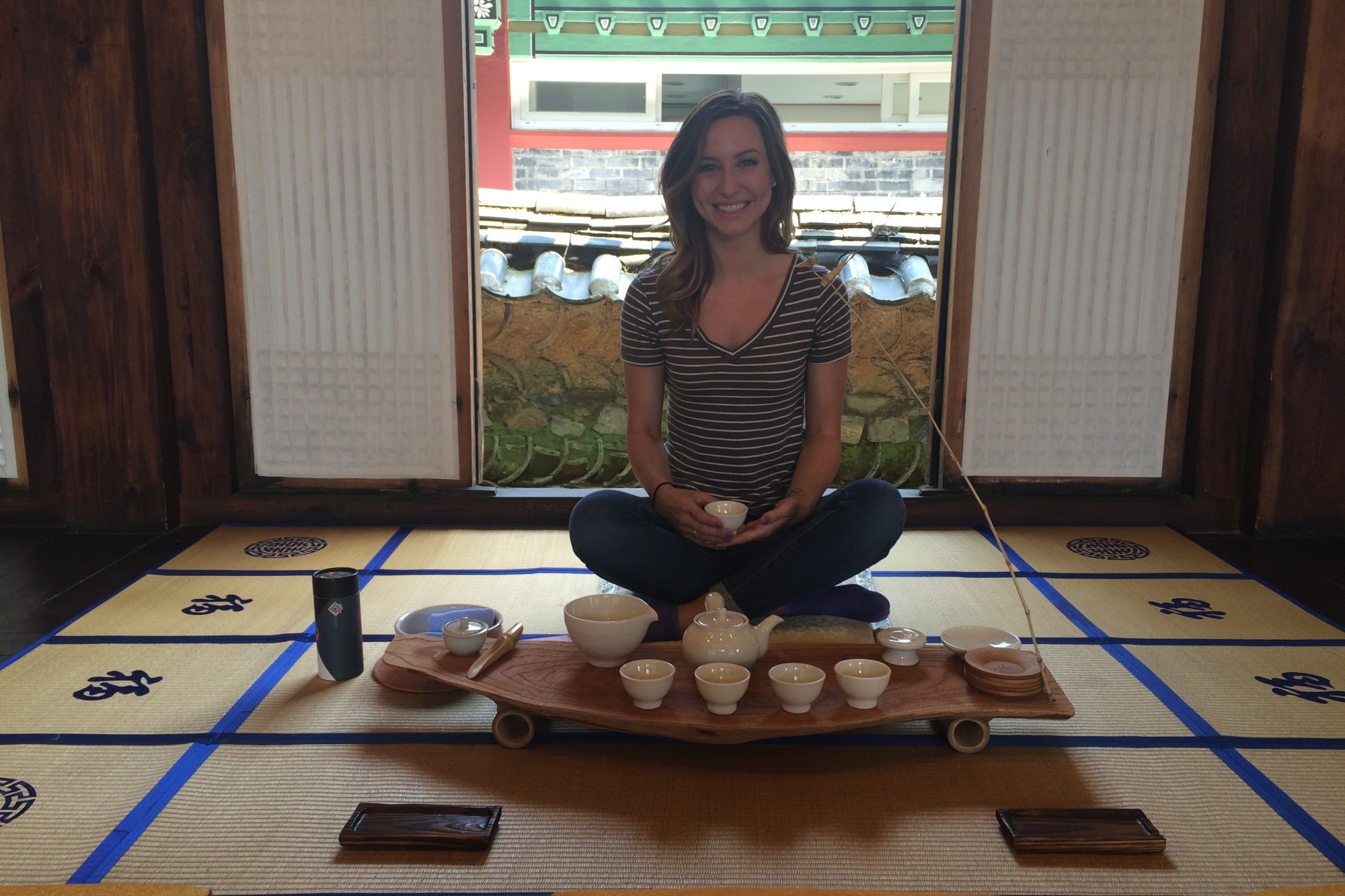 a woman in a striped shirt sits cross-legged on the floor in front of a tea set