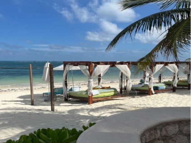 The image shows a serene beachfront with cabana beds, white drapes and a clear blue sky, evoking a sense of relaxation and vacation.
