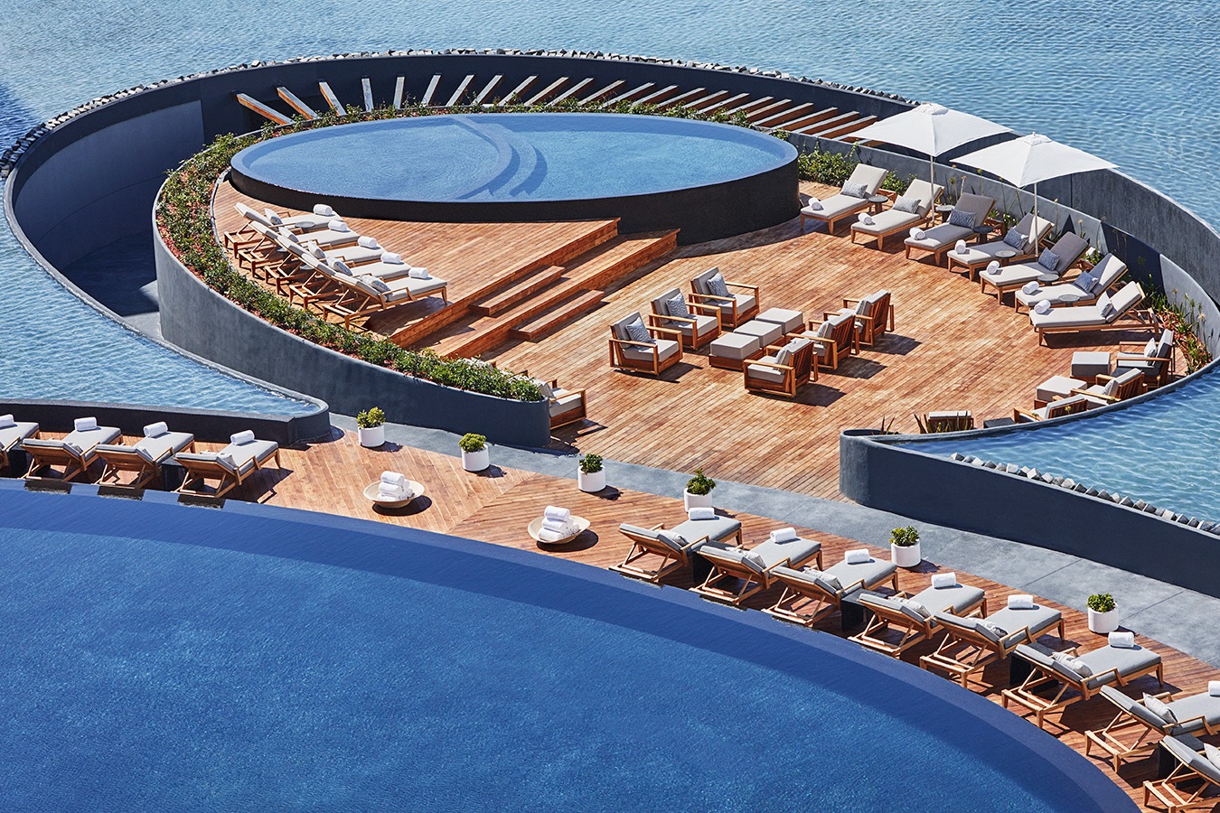 aerial view of a complex made up of oval pools centered on a sleek wooden deck