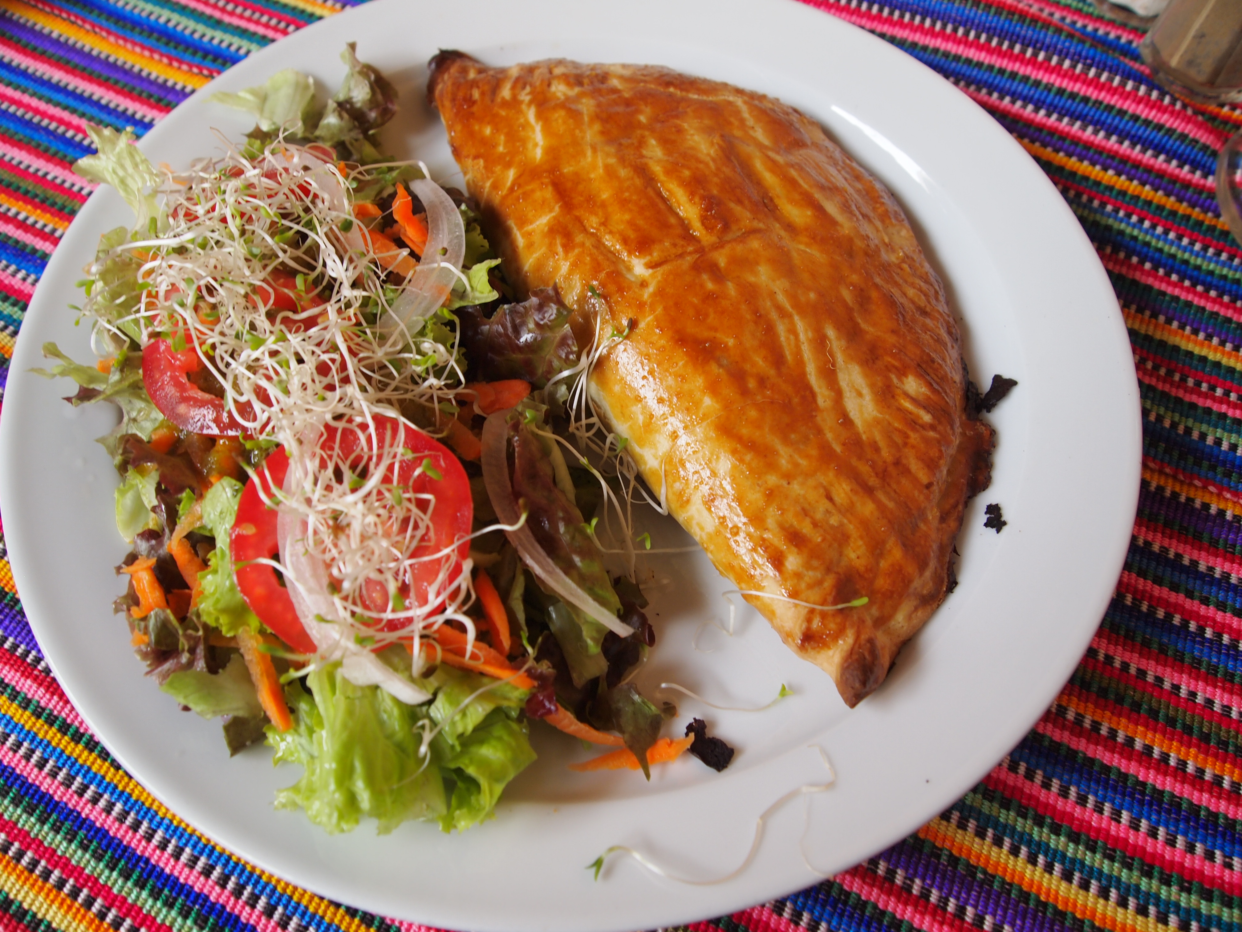 A plate of food with a large omelette and a side salad on a colorful woven tablecloth.