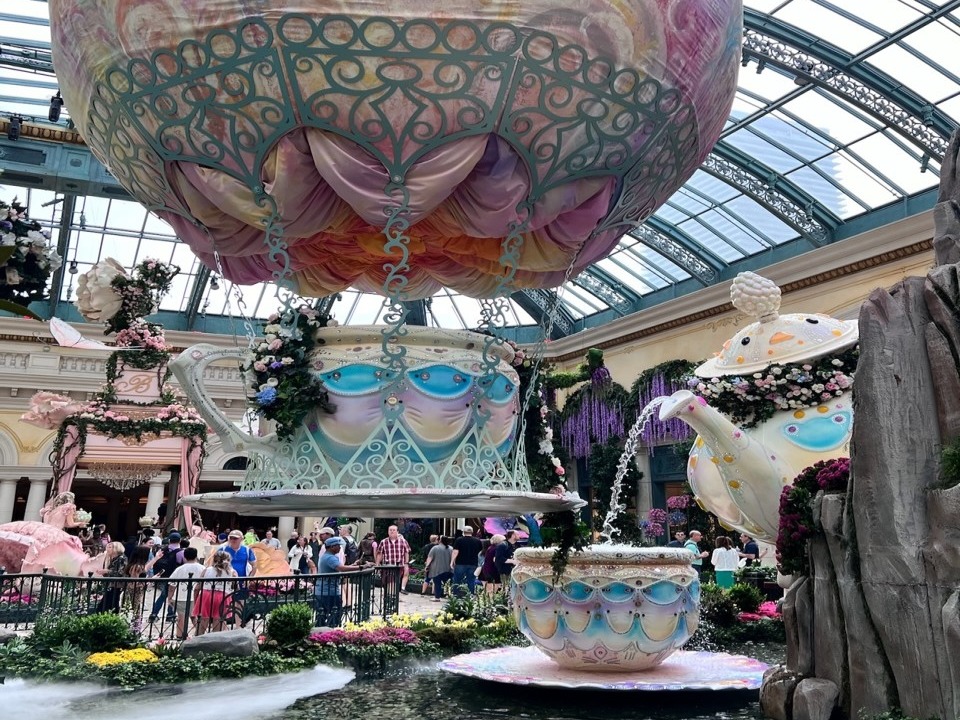 The image features an elaborate hot air balloon display within a glass-domed conservatory, observed by onlookers below.