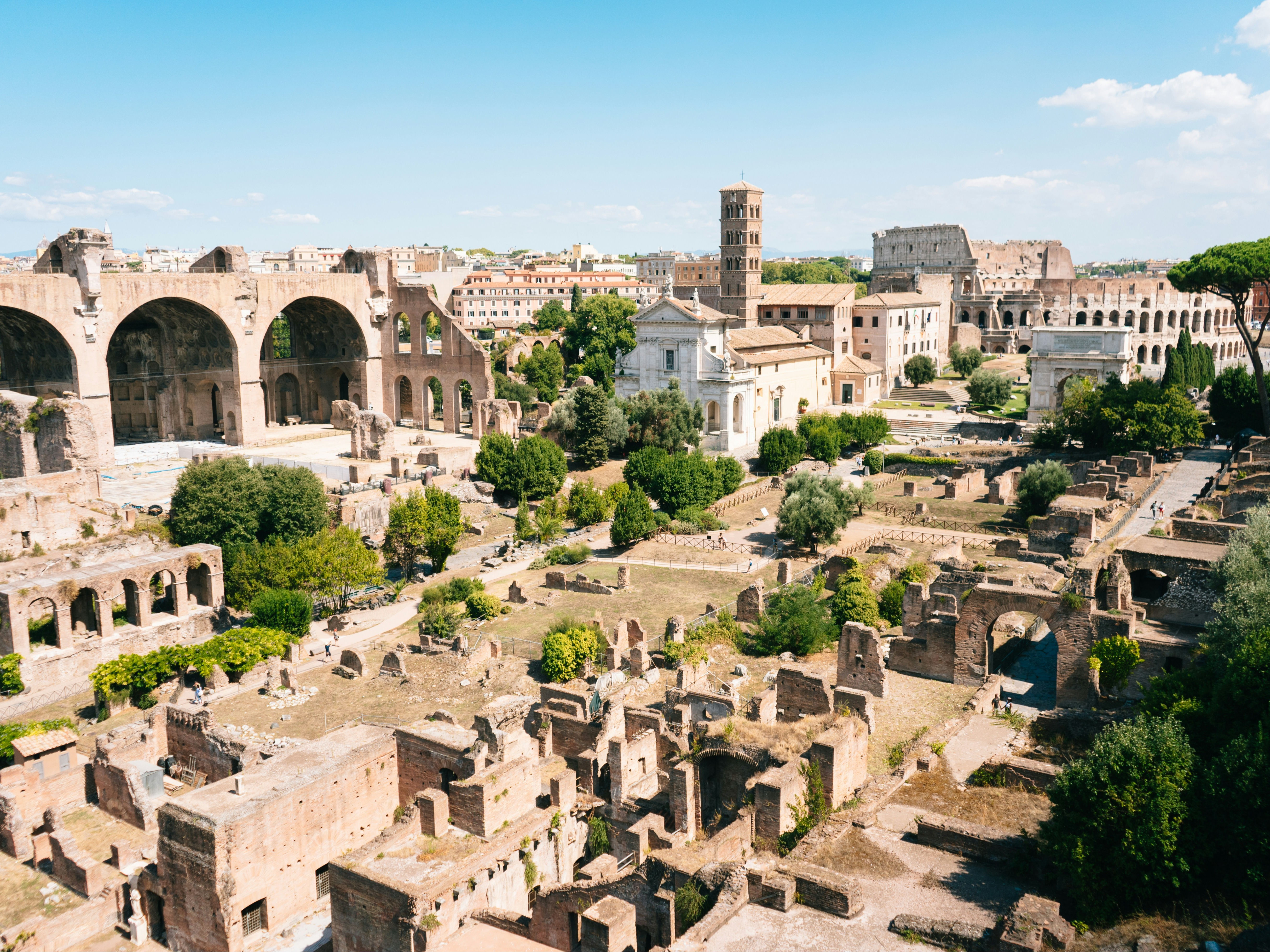 The image shows the ancient Roman Forum with ruins and arches under a clear blue sky.