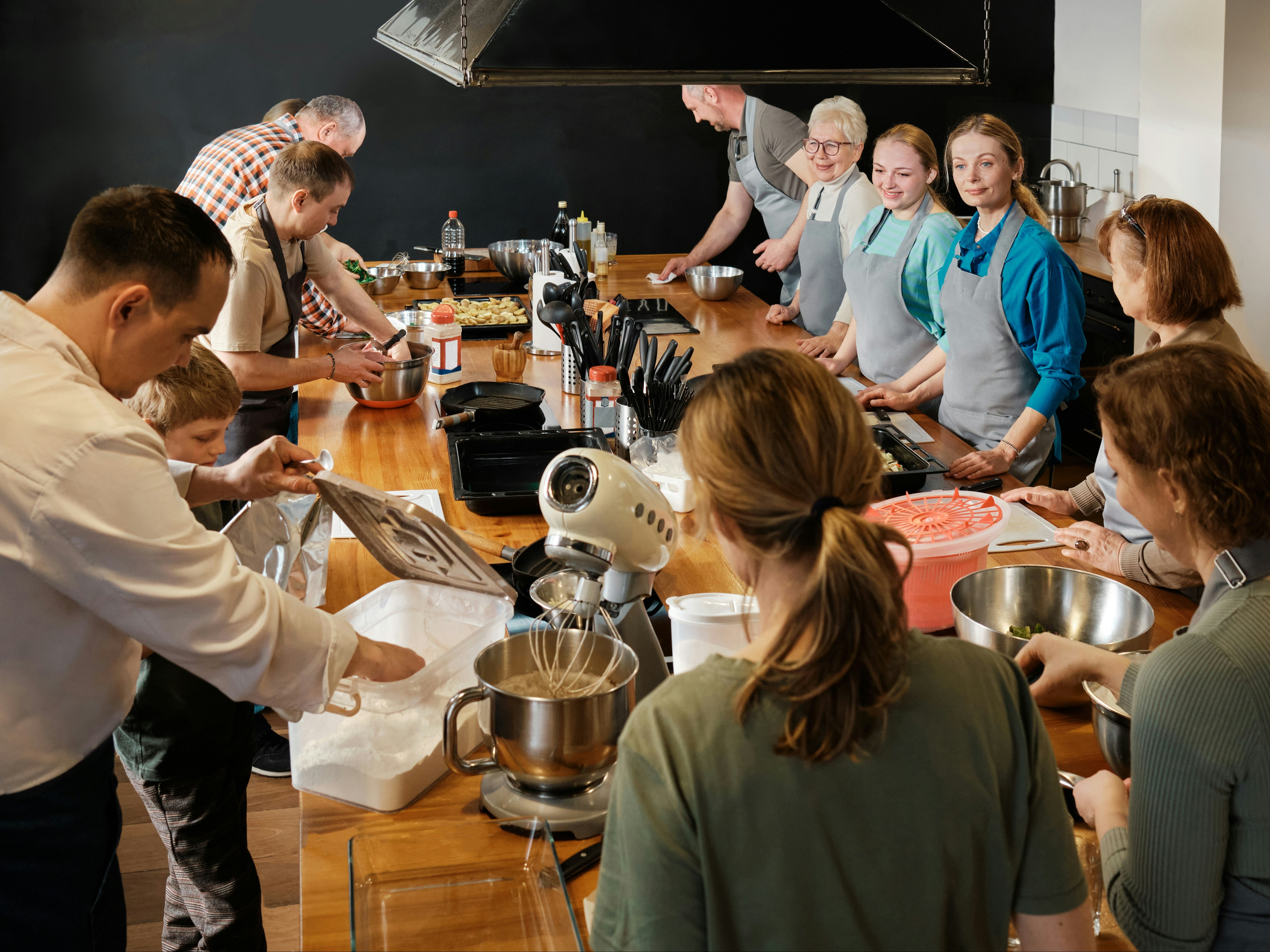 The image captures a bustling kitchen scene with individuals engaged in culinary tasks during a cooking class.