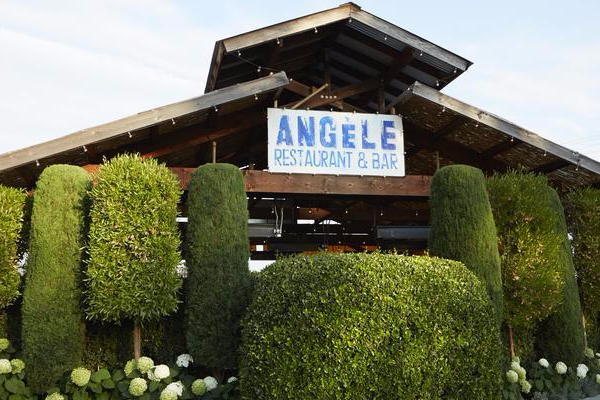 A wooden building with a sign that reads "Angèle Restaurant & Bar" with manicured hedges out front.