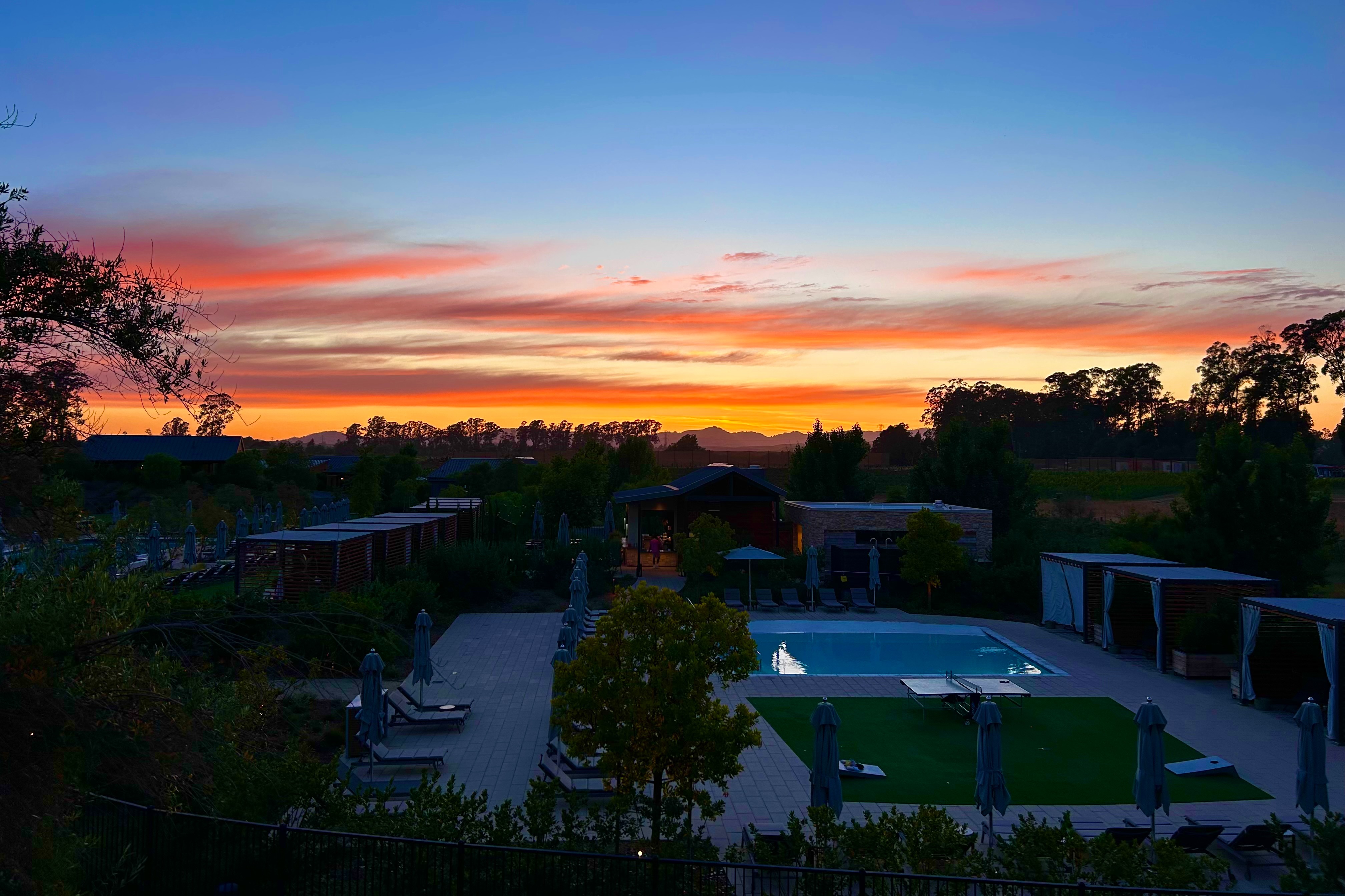 A sunset over a pool with trees in the distance at Solage Calistoga.