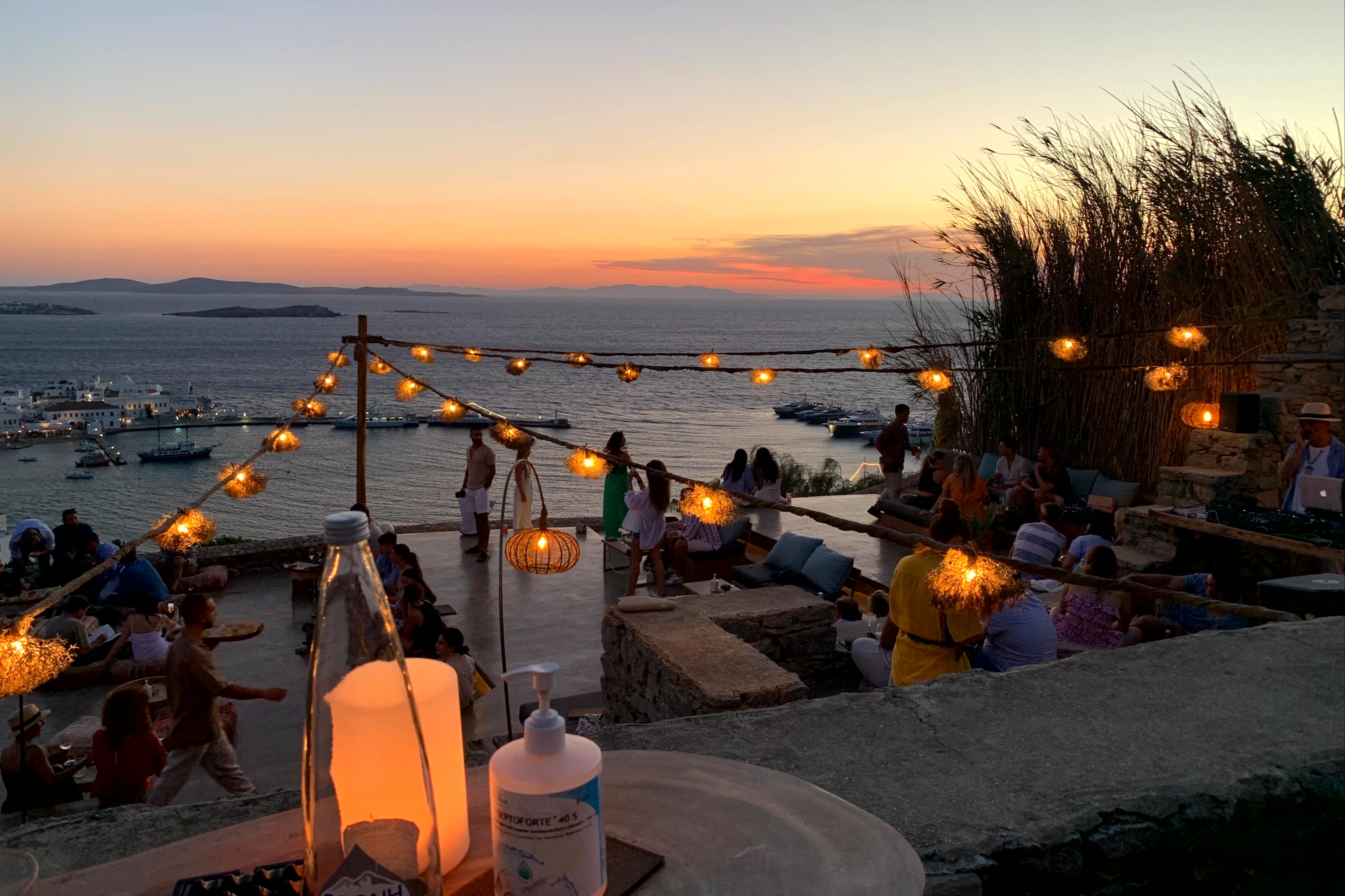 A patio view of string lights reaching toward a beach shore at dusk over the water.