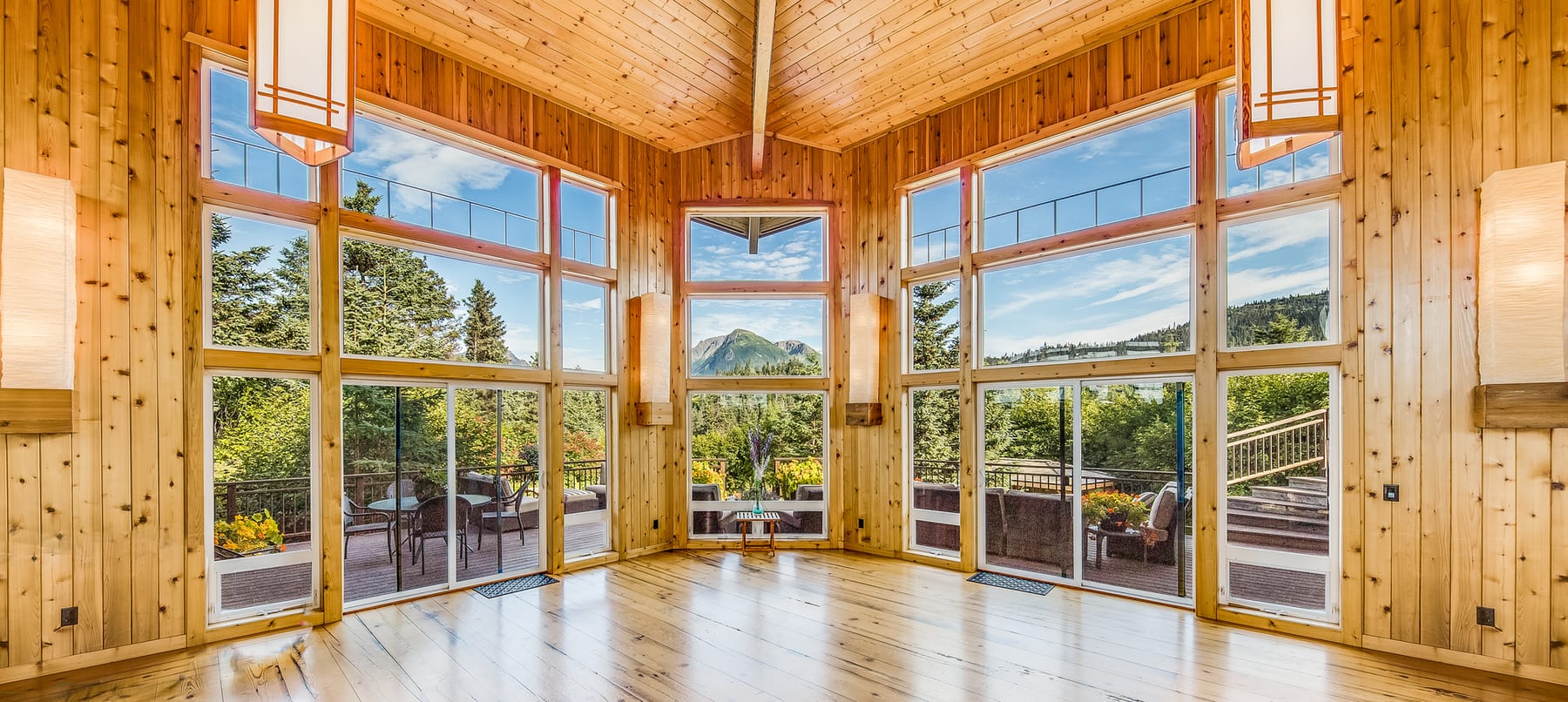 A lodge with a rustic wooden interior, big windows and views of forests and mountains outside.