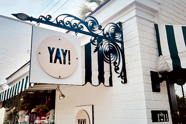 Shop with cute display sign saying "Yay!" against a white brick building with black and white awning.